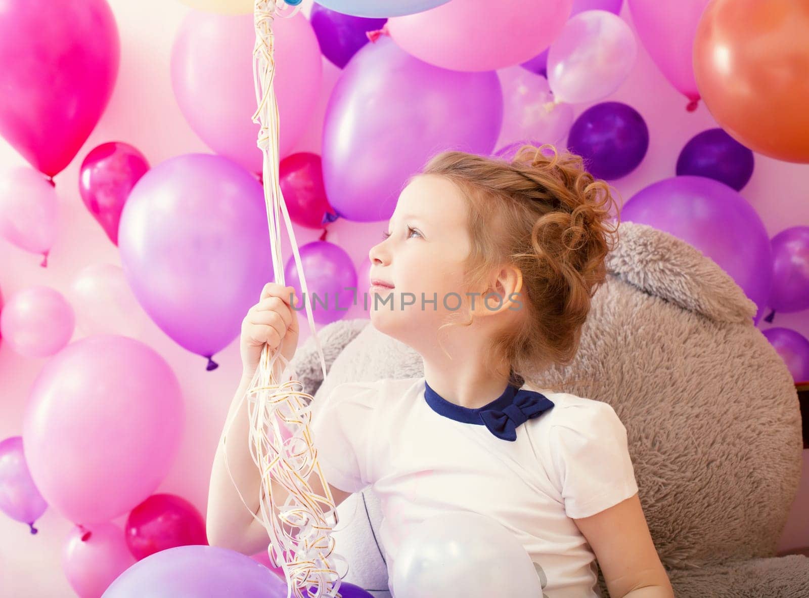 Sympathetic little girl posing holding bunch of balloons