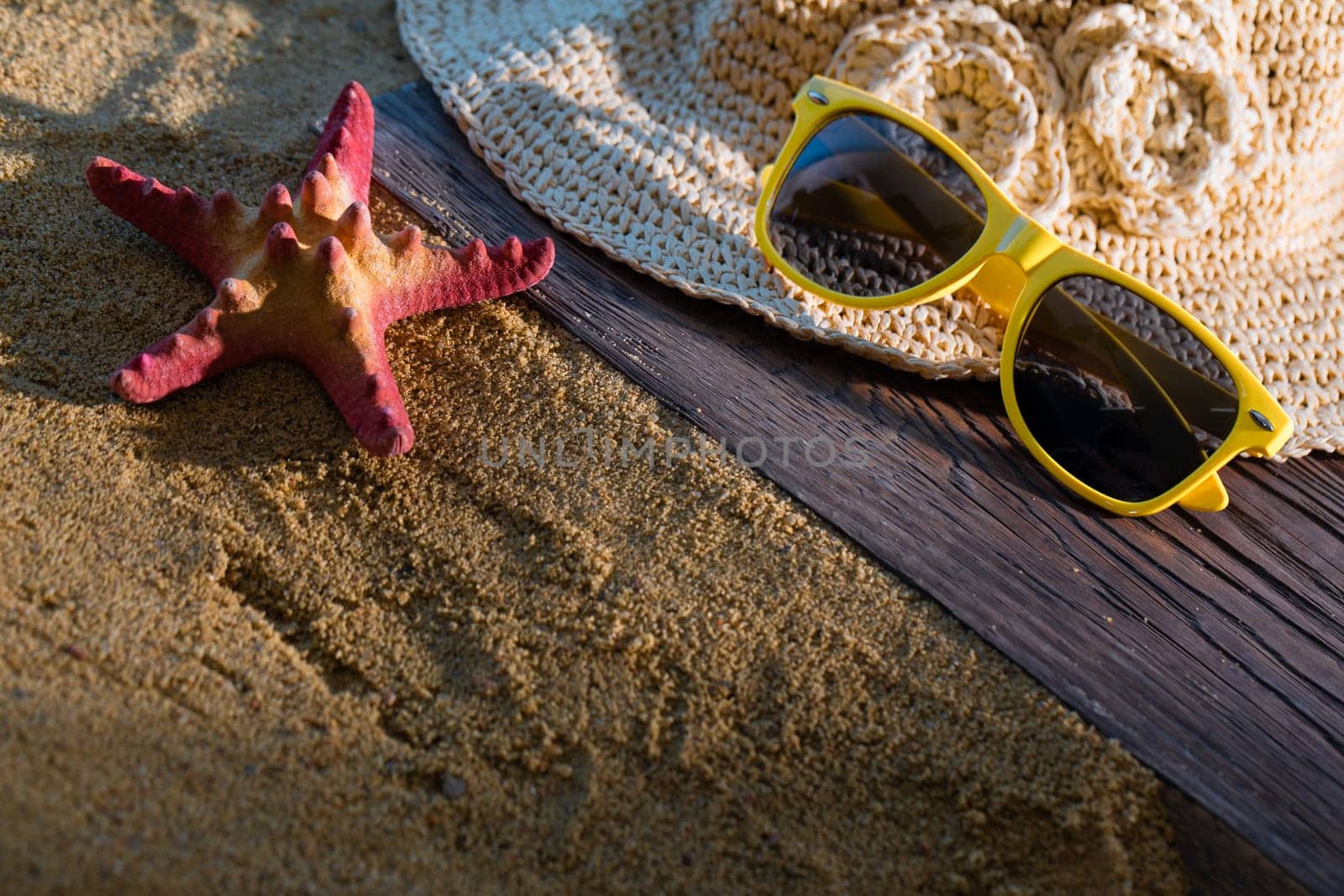 A summer hat and sunglasses lie on the sandy coast of the sea beach.