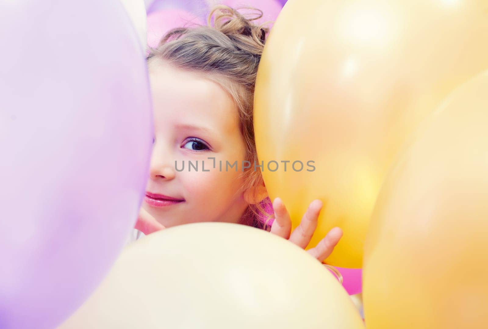 Portrait of cute little girl peeking out from behind balloons