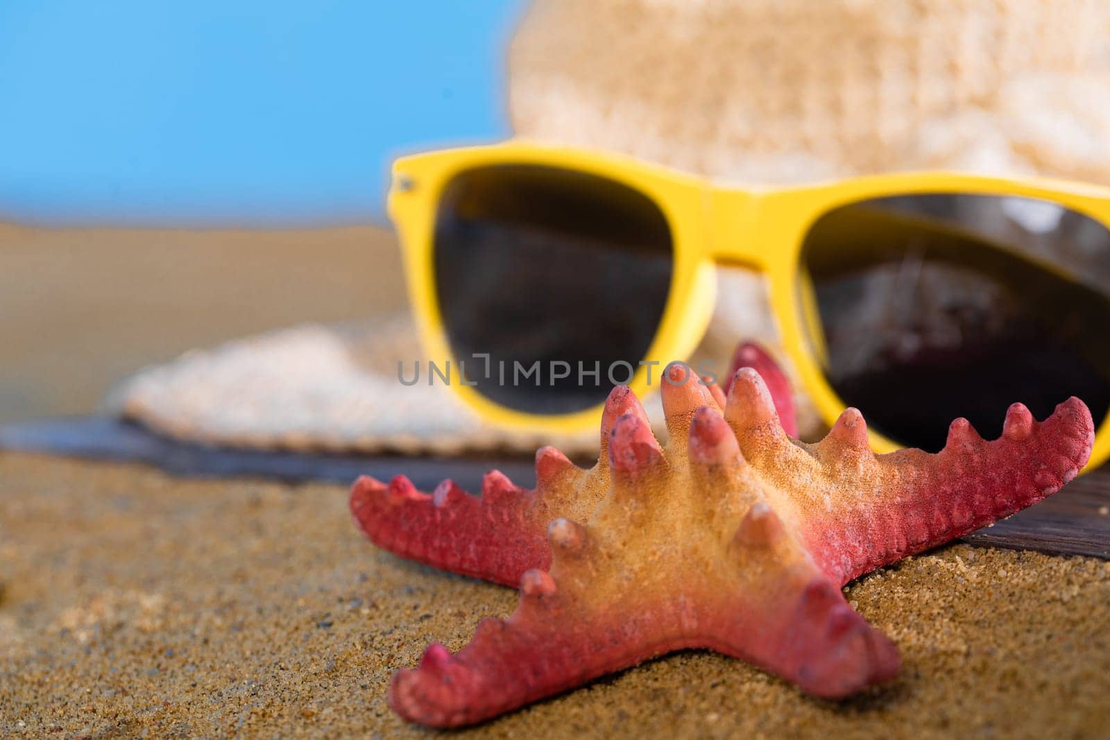Blue sky over the sea beach. A summer hat and sunglasses lie on the sandy coast of the sea beach.