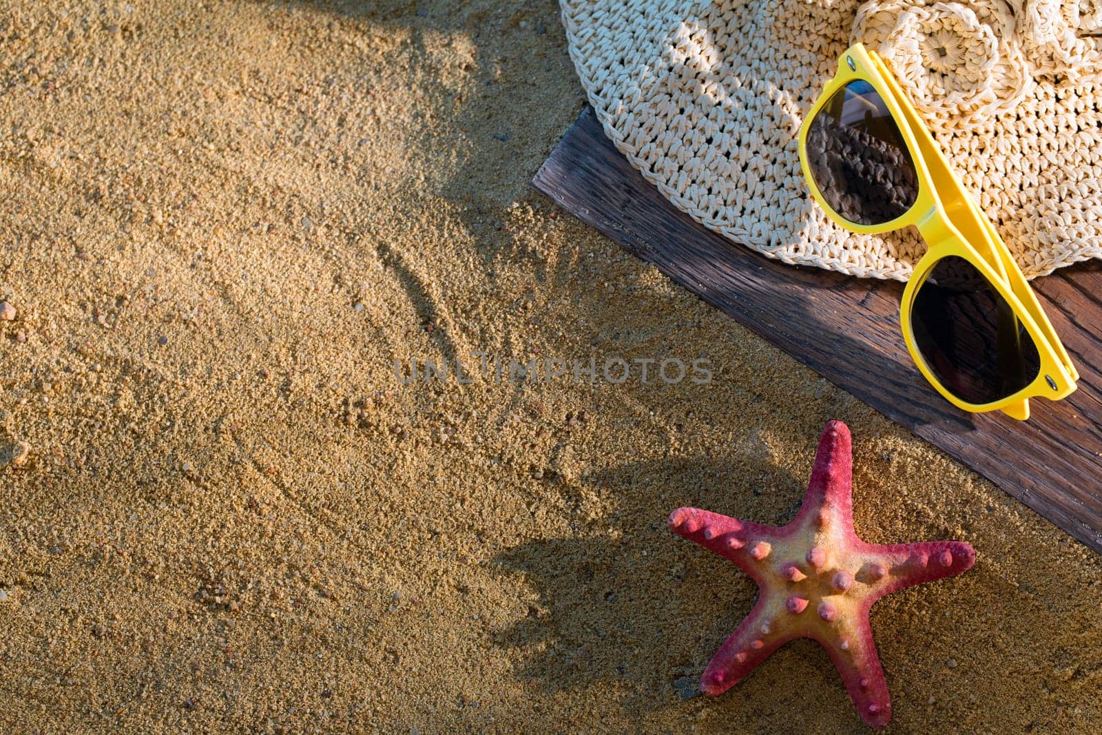 A summer hat and sunglasses lie on the sandy coast of the sea beach.