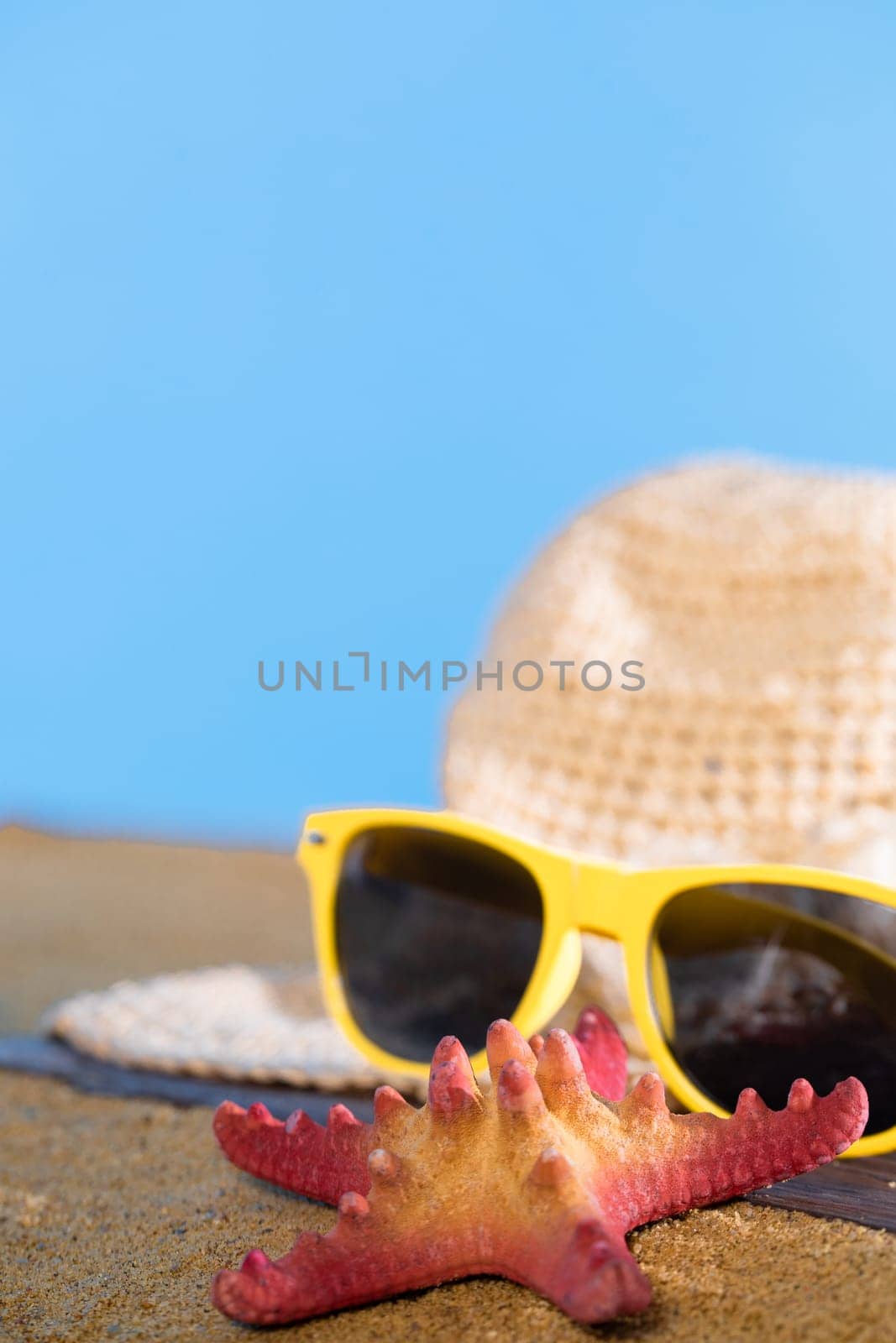 Hat and sunglasses lie on the sea beach against the blue sky. Sunny coast on a sunny morning. by fotodrobik