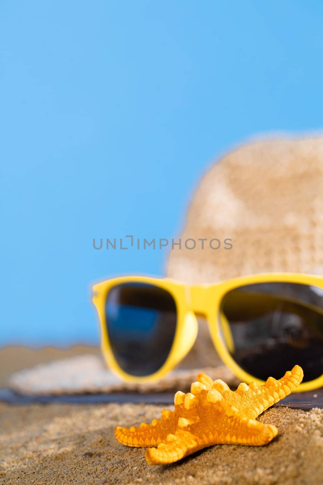 Hat and sunglasses lie on the sea beach against the blue sky. Sunny coast on a sunny morning. by fotodrobik