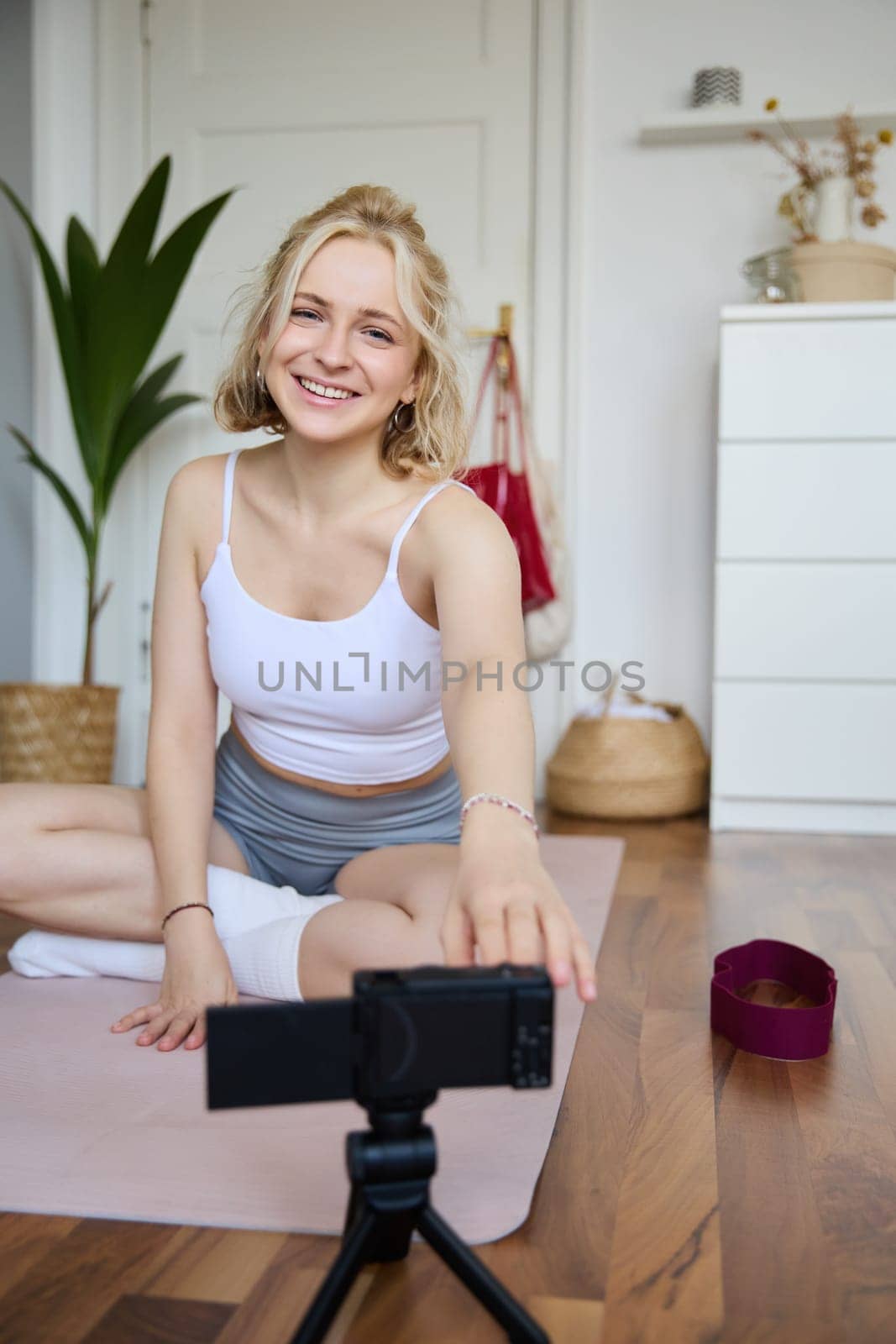 Vertical shot of athletic, fitness woman recording video of herself on digital camera, creating content for social media about workout and home exercises.