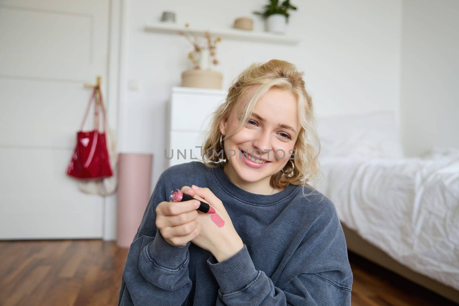 Portrait of beautiful young woman, content creator for social media, sitting in front of digital camera, recording video about makeup, showing lipstick swatches on her skin.