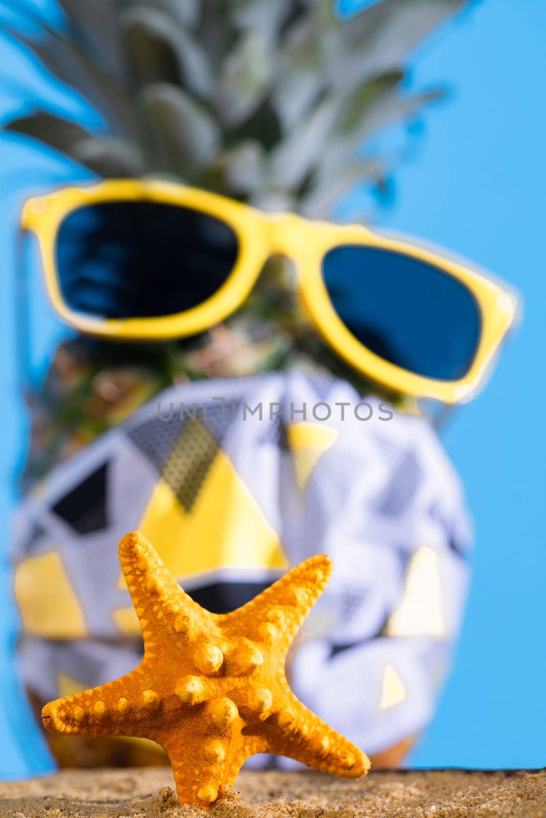 Pineapple in sun glasses and a protective mask stands on the sandy sea beach. by fotodrobik