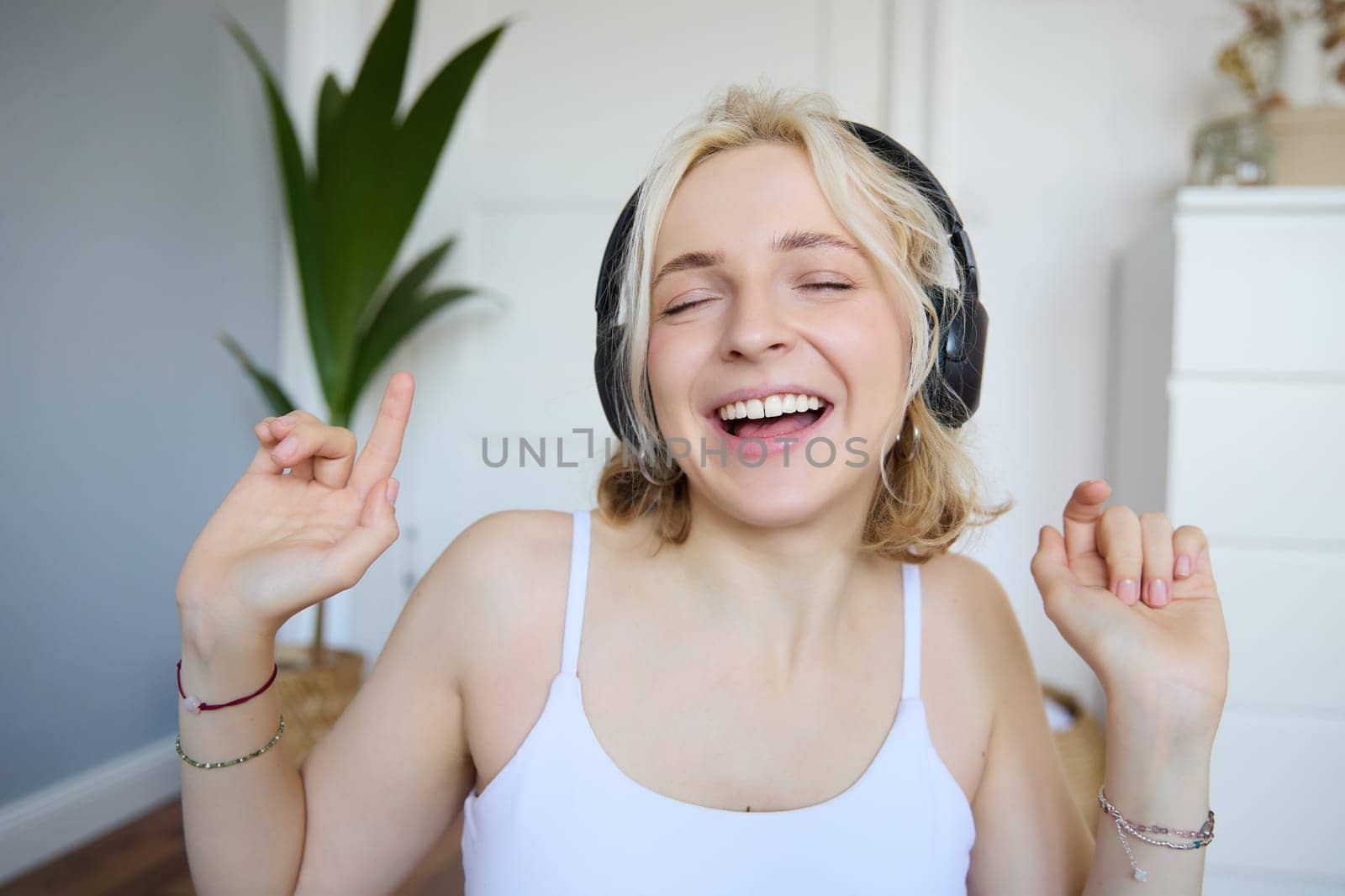 Dancing girl listens to music, woman wears wireless headphones and enjoys sound quality, sings by Benzoix