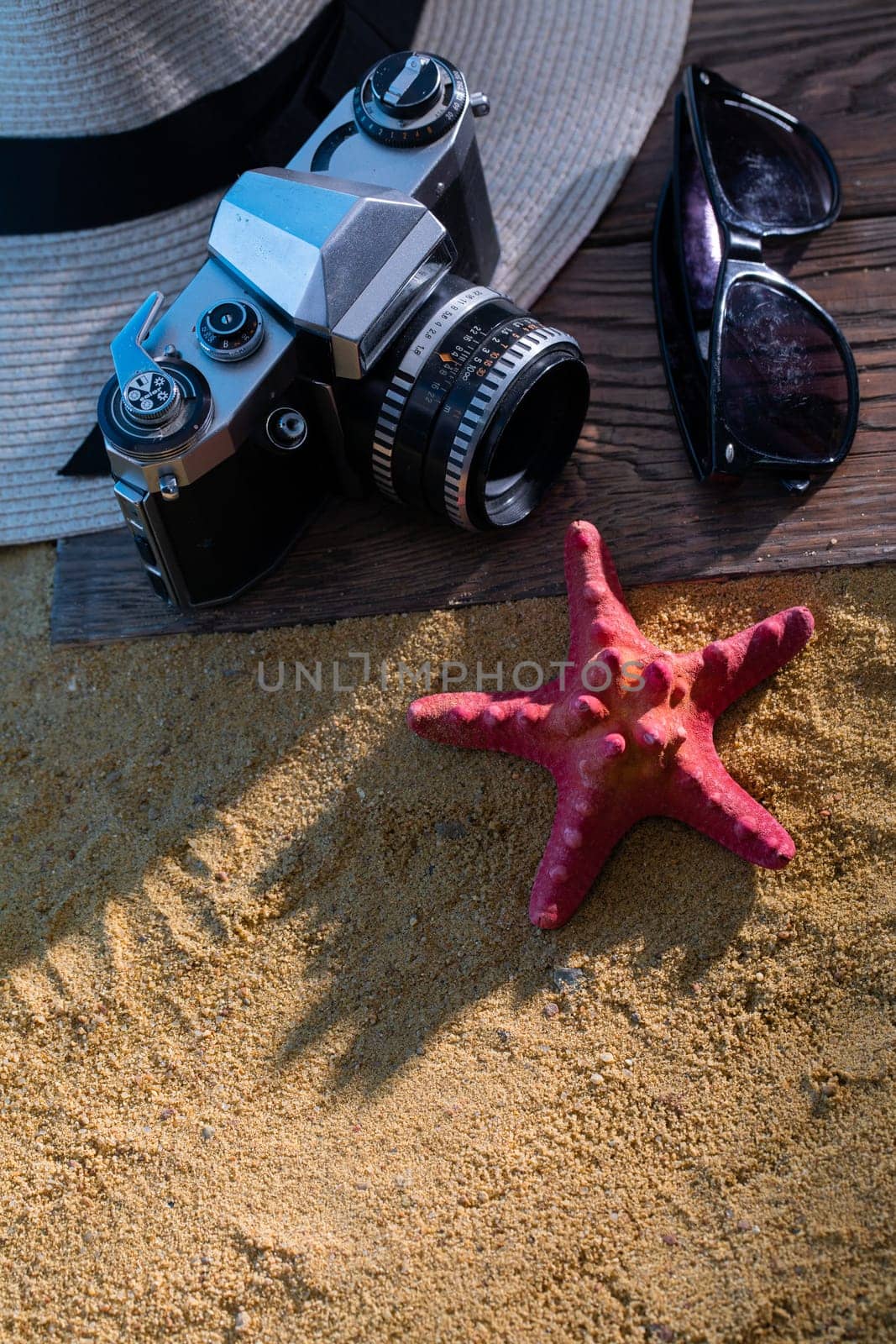 Old photographic film camera. Sunglasses. Sandy sea beach. Summer hat.