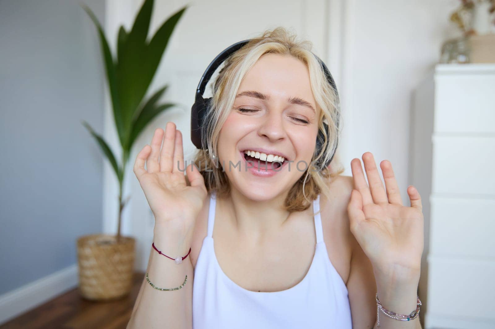 Close up portrait of candid, happy young woman in headphones, singing and listening to music at home.