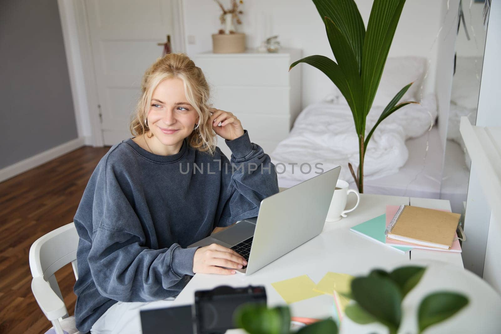 Portrait of woman sitting at desk with laptop, recording video of herself on laptop, making lifestyle video for social media account.