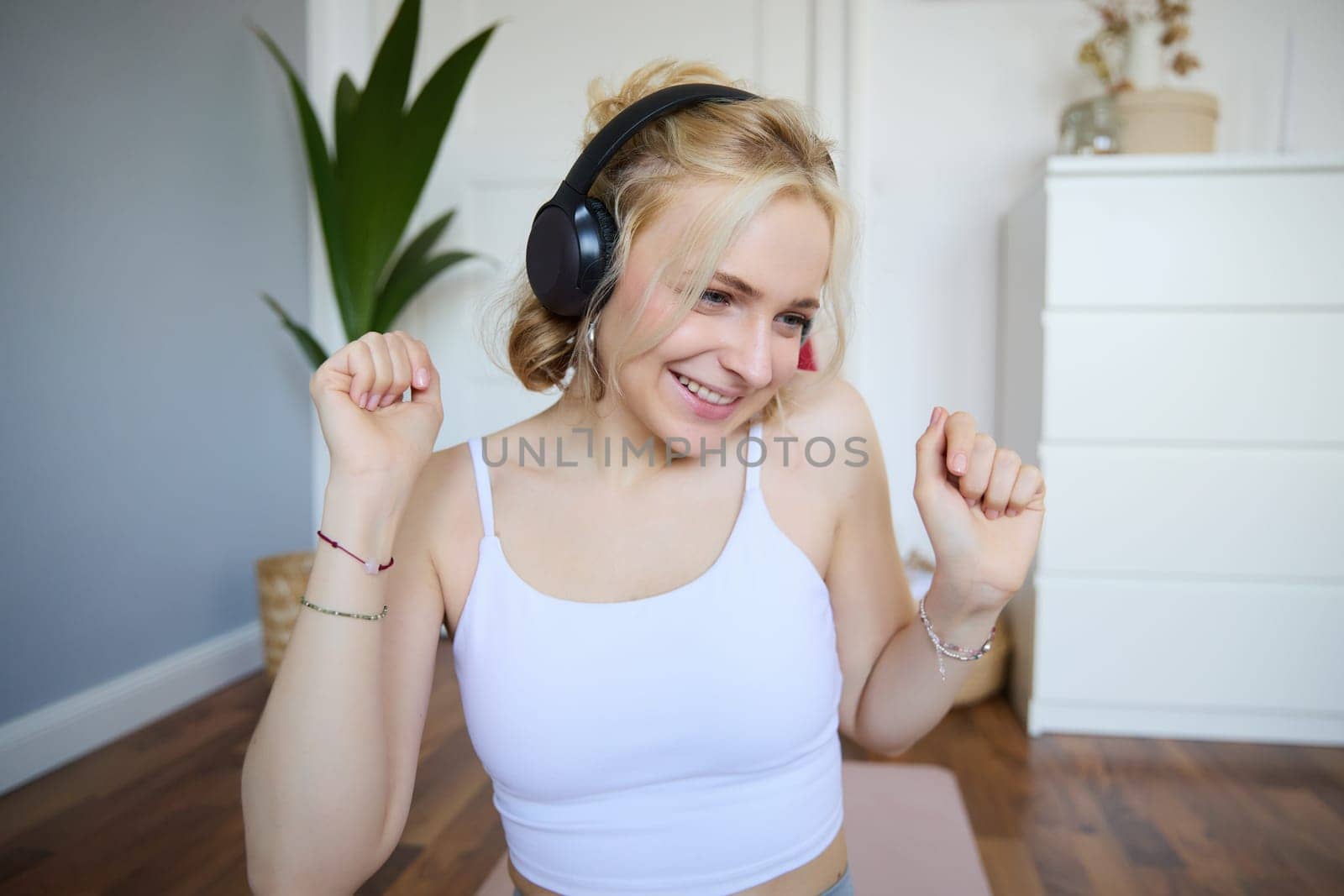Portrait of beautiful blond girl, fitness woman dancing in wireless headphones, enjoying working out tuning into favourite song.