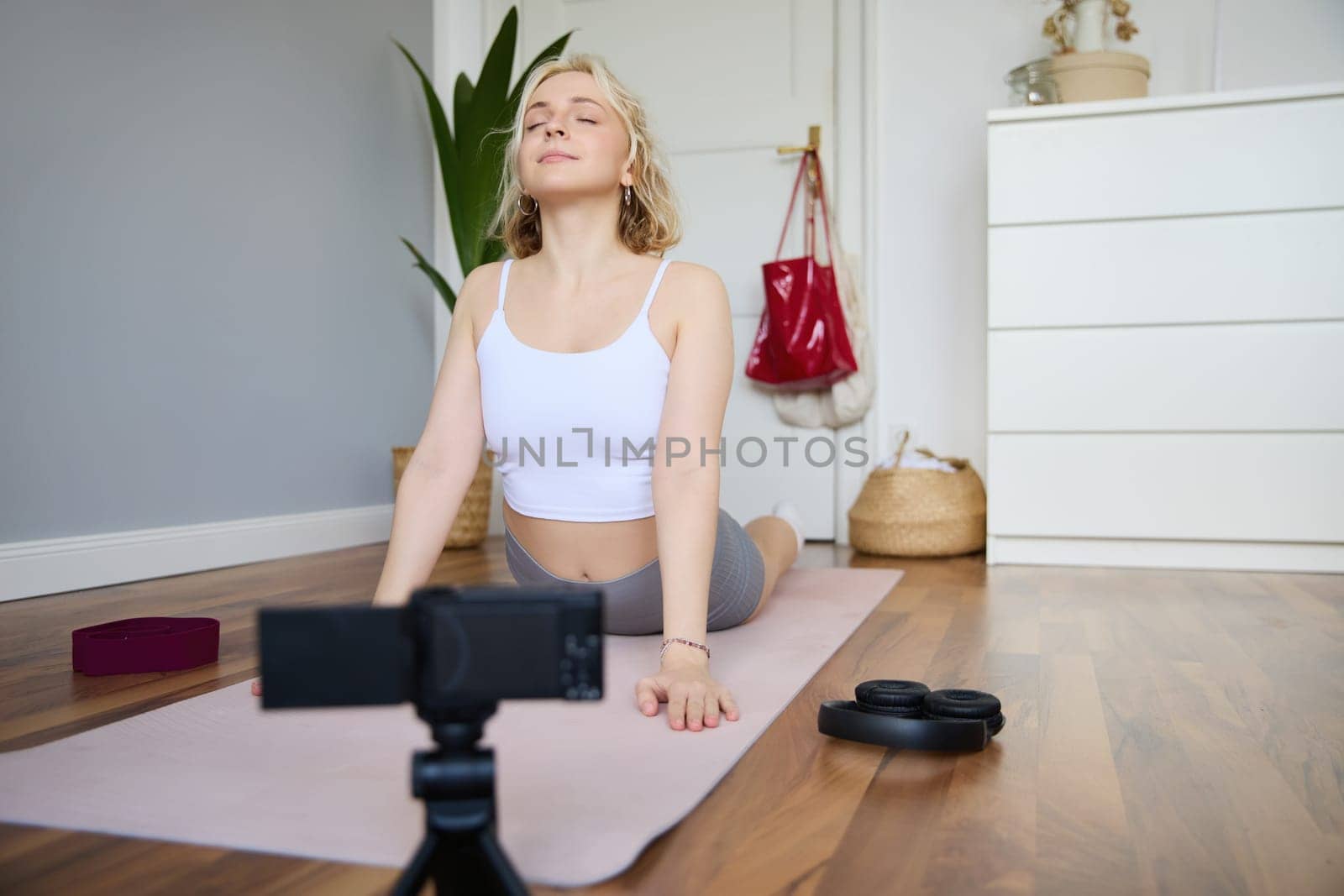 Portrait of young blogger, yoga content creator, showing exercises, recording video of herself working out at home on rubber mat.