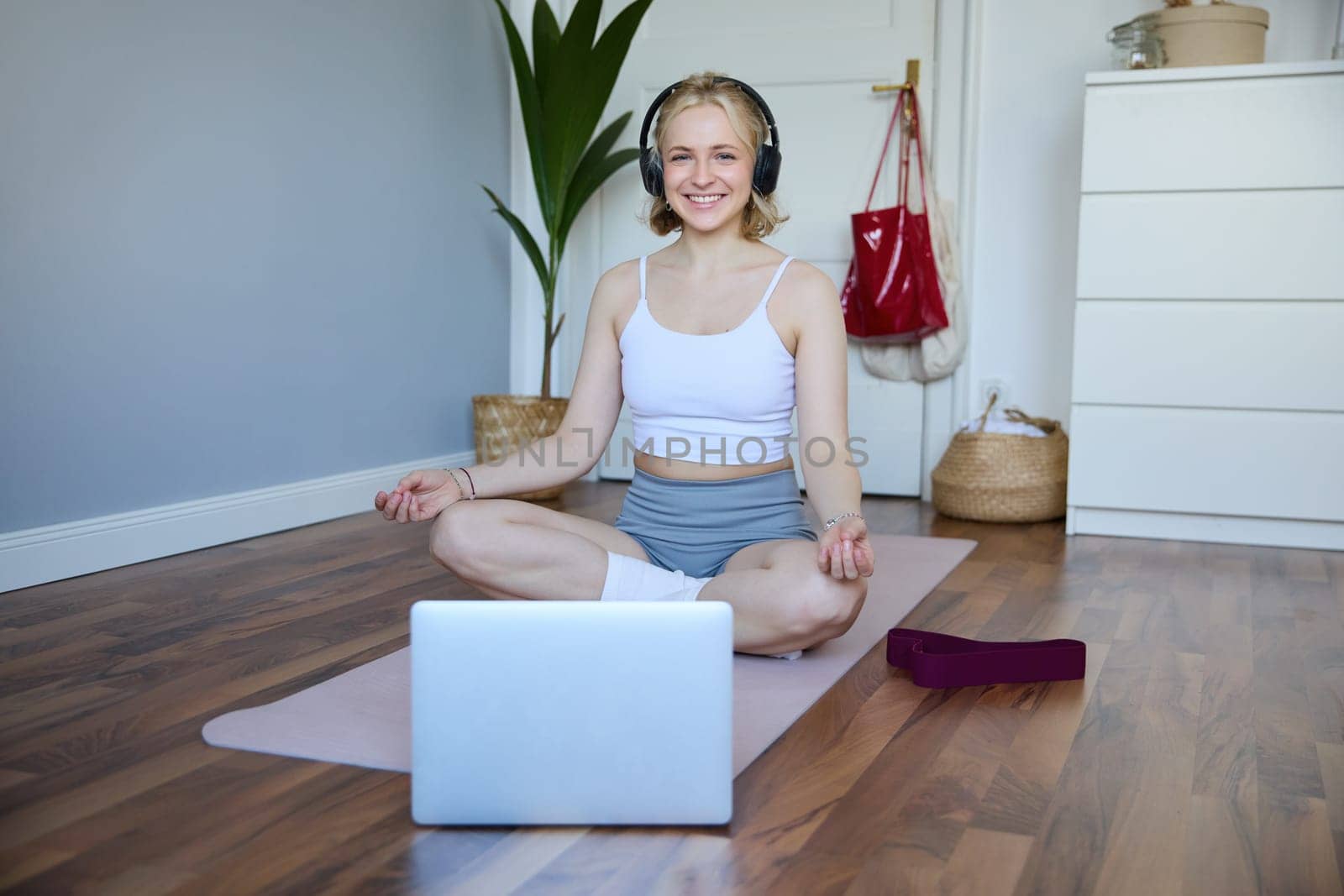 Portrait of fit and healthy woman at home, practice yoga, sitting on rubber mat, listening to instructions online, using meditation music to relax, following guidance on laptop.