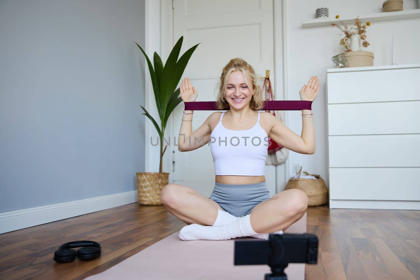 Portrait of young athletic woman recording home workout video, shooting content for sport fitness vlog, using resistance band and digital camera by Benzoix