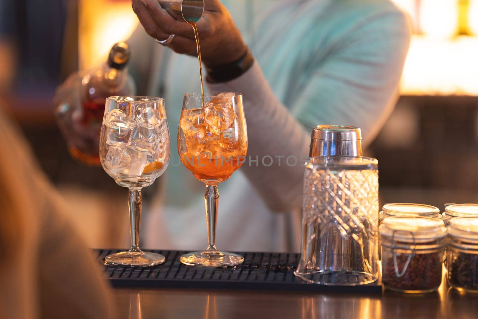 A man is pouring a drink into two glasses on a bar by Studia72
