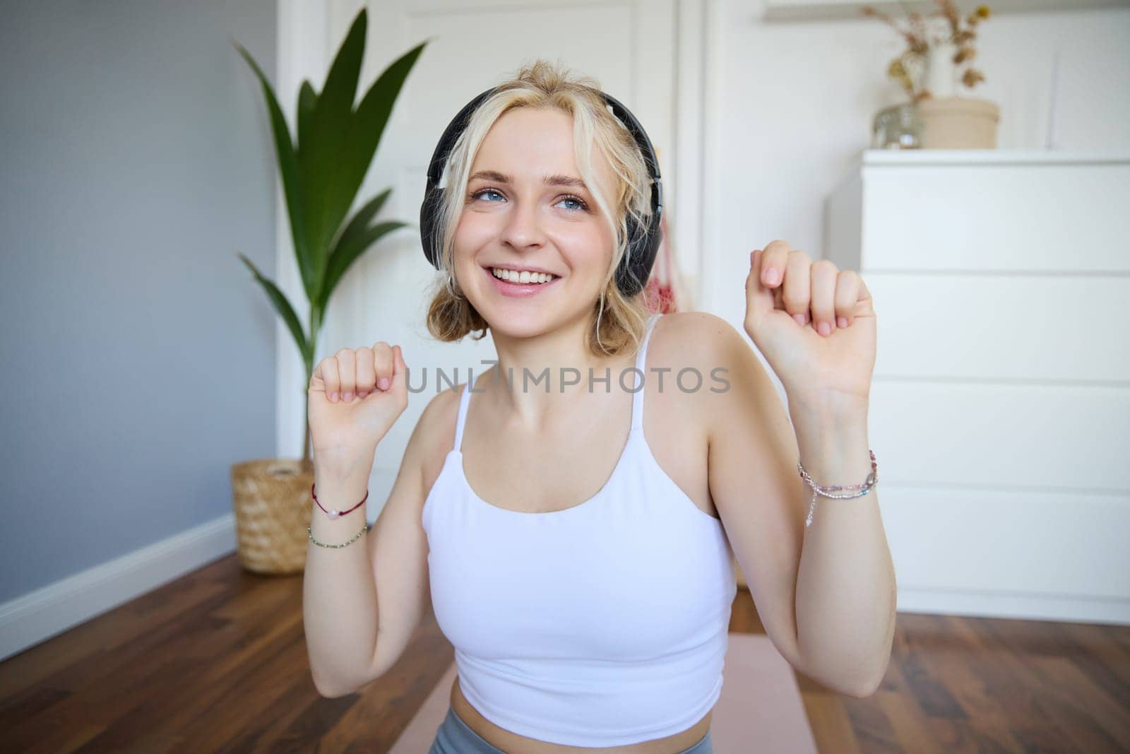 Close up of athletic young woman, cute female model in wireless headphones, dancing to favorite song, listens to music in earphones.