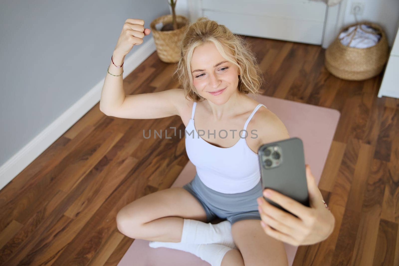 Portrait of young sporty woman taking selfie during workout training, content creator takes photos, shows muscles on camera, flexing biceps by Benzoix