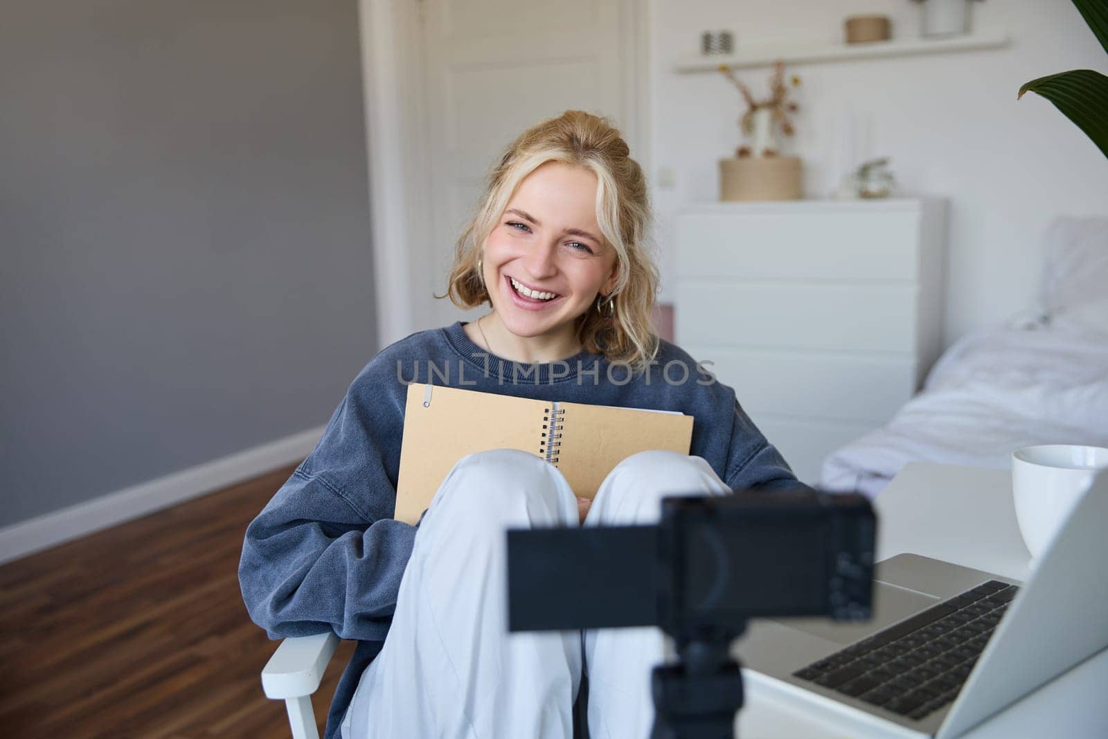 Portrait of cute, smiling young social media content creator, girl records video on digital camera and stabiliser, holds notebook, talks to audience, vlogging in her room.