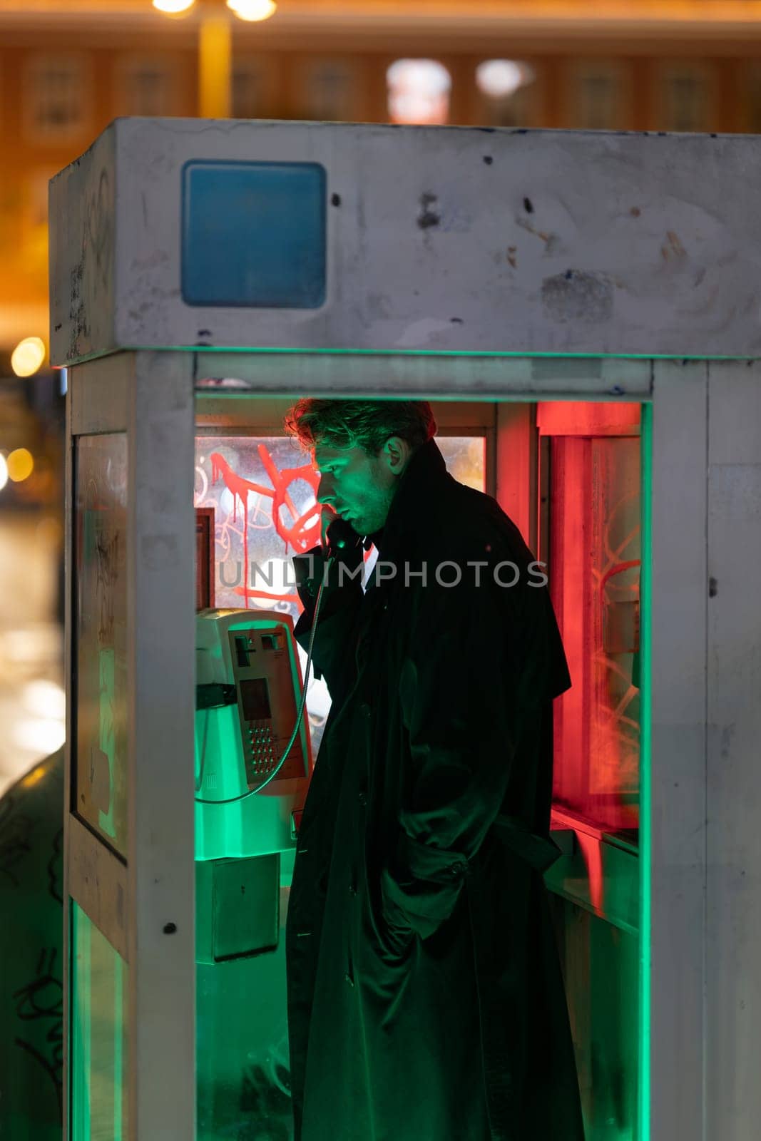 A man is talking on a phone in a booth. The booth is in a dimly lit area
