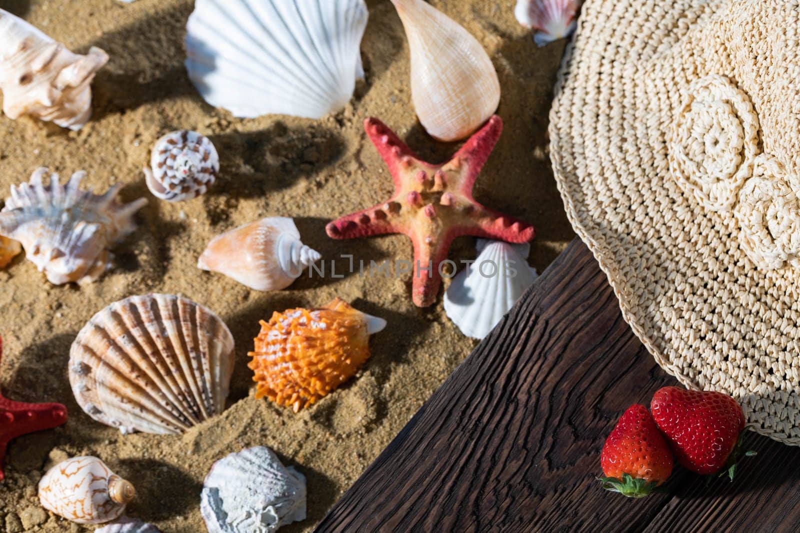 Sea beach full of various shells. Sandy beach. Two ripe strawberries. Summer hat.