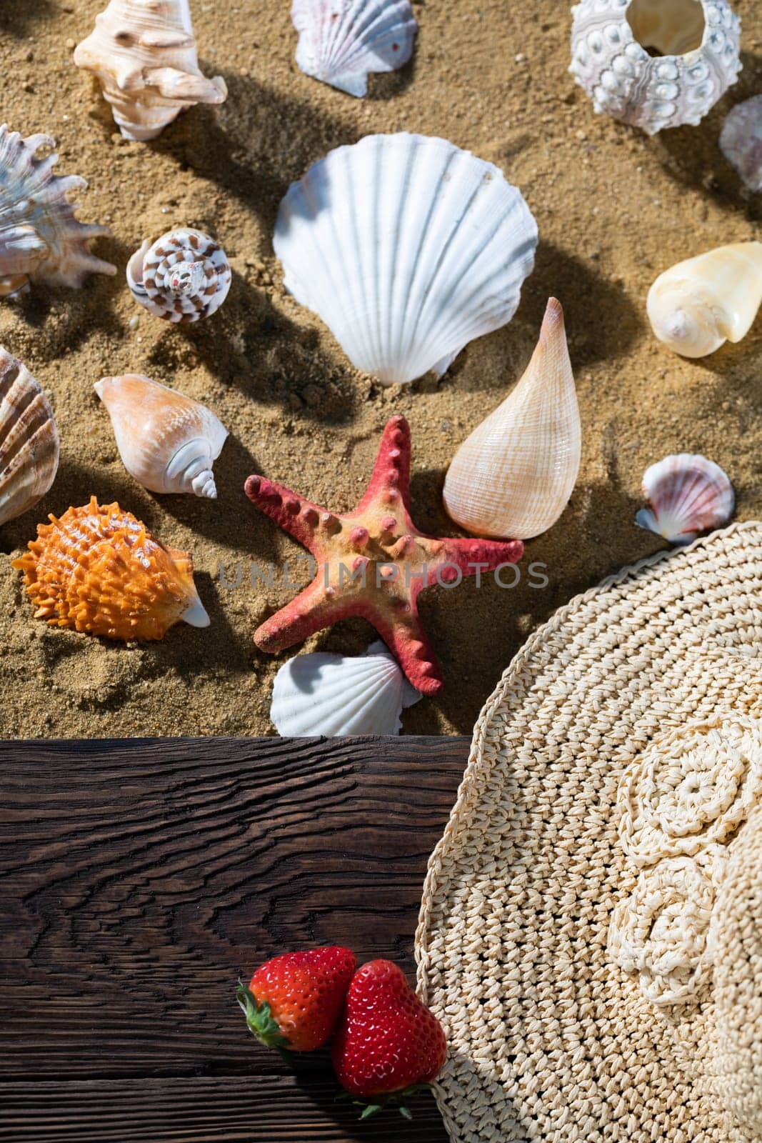 Sea beach full of various shells. Sandy beach. Two ripe strawberries. Summer hat.