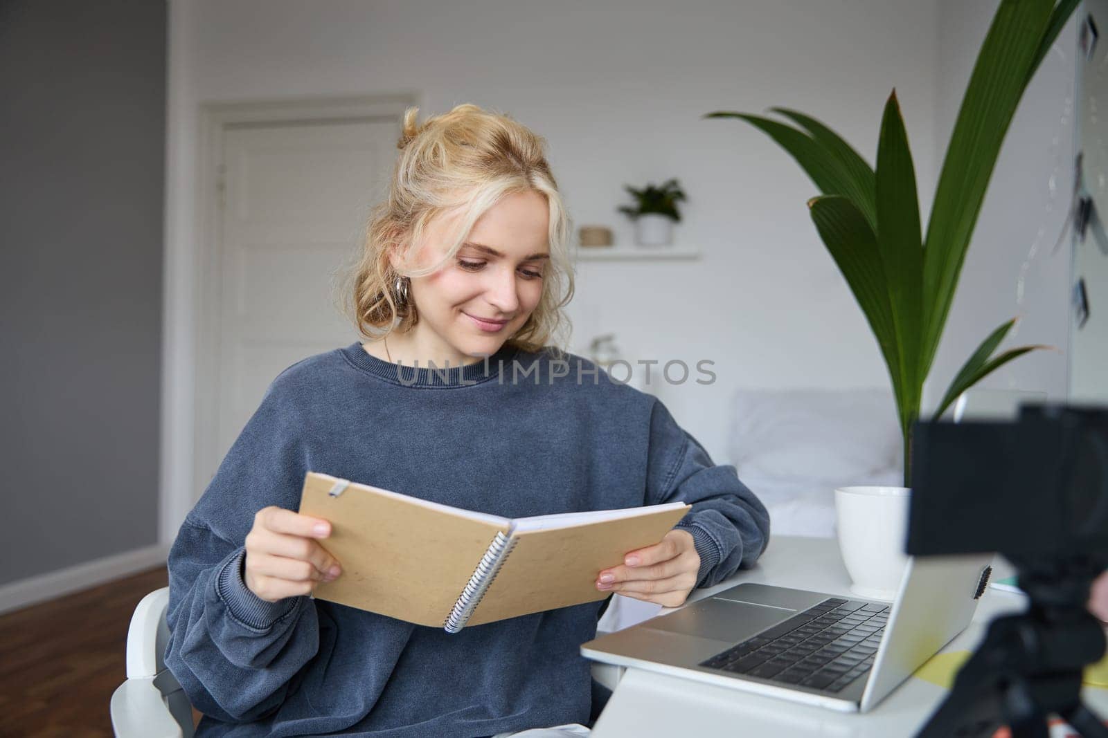 Portrait of young woman using digital camera and laptop, studying, connect to online live stream, records video for vlog, creating content, holding notebook, sitting in room.