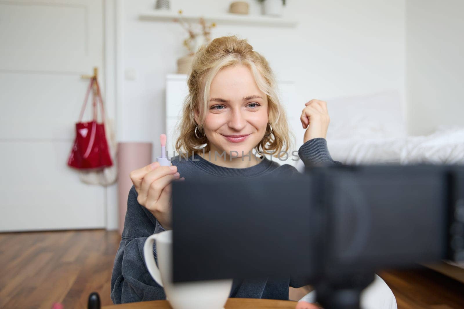 Image of happy, beautiful young social media influencer, female vlogger records a video on digital camera, tutorial on how to put makeup, getting ready for going out, talking to followers.