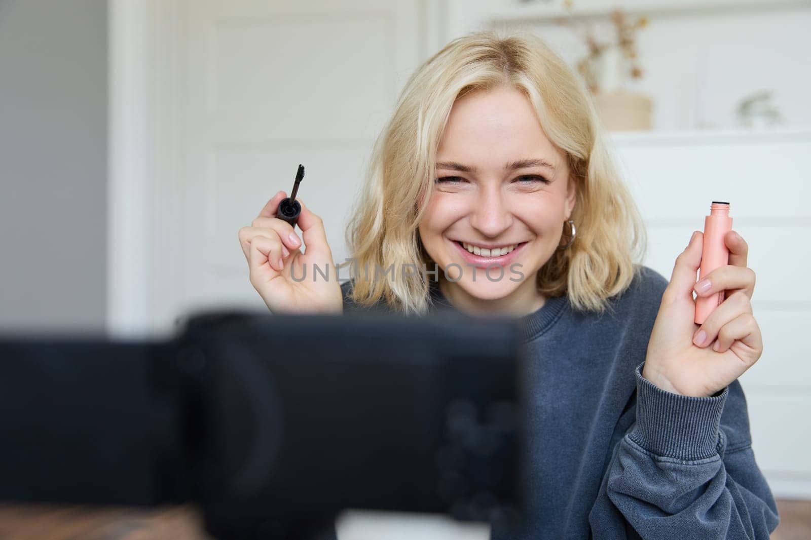 Portrait of beauty blogger, woman records video on camera in her room, shows makeup beauty products, talks about cosmetics in vlog, makes lifestyle content for followers on social media.