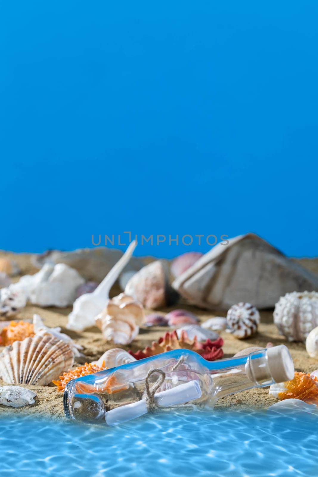 A glass bottle with a letter washed up on the beach shore. Sea beach full of shells and sand. Blue sky. Clean water. by fotodrobik