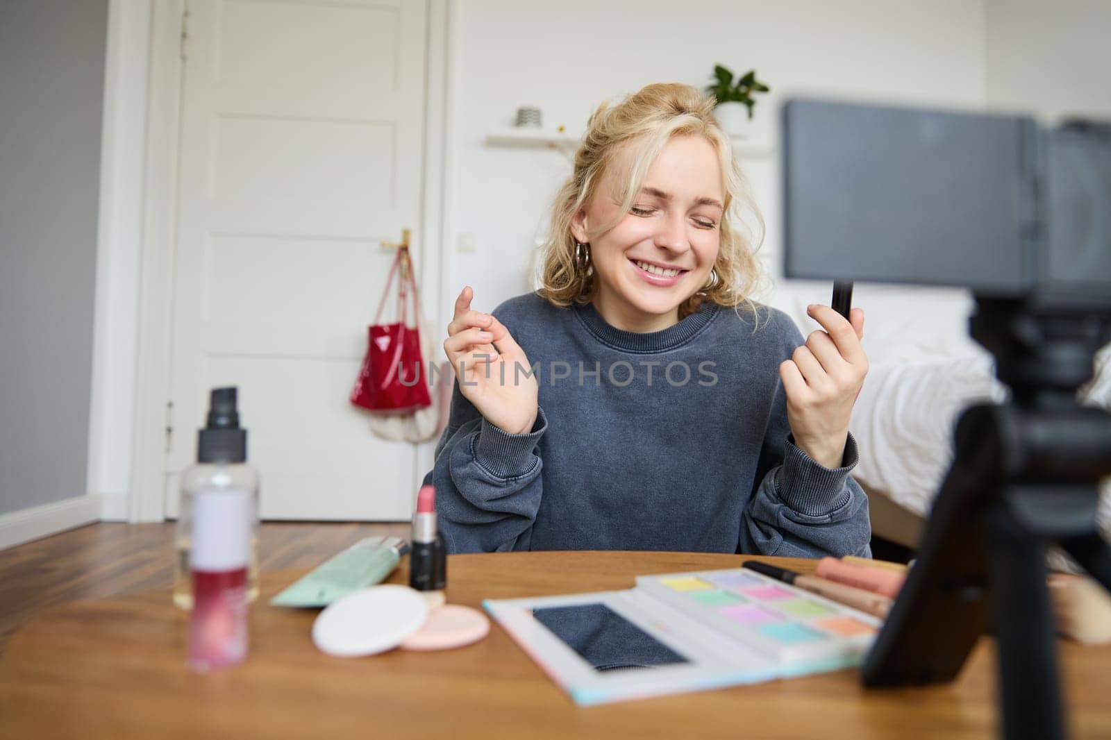 Portrait of young content maker, woman blogger recording a video on digital camera, showing lipstick colour to her followers, creating lifestyle vlog for social media account.