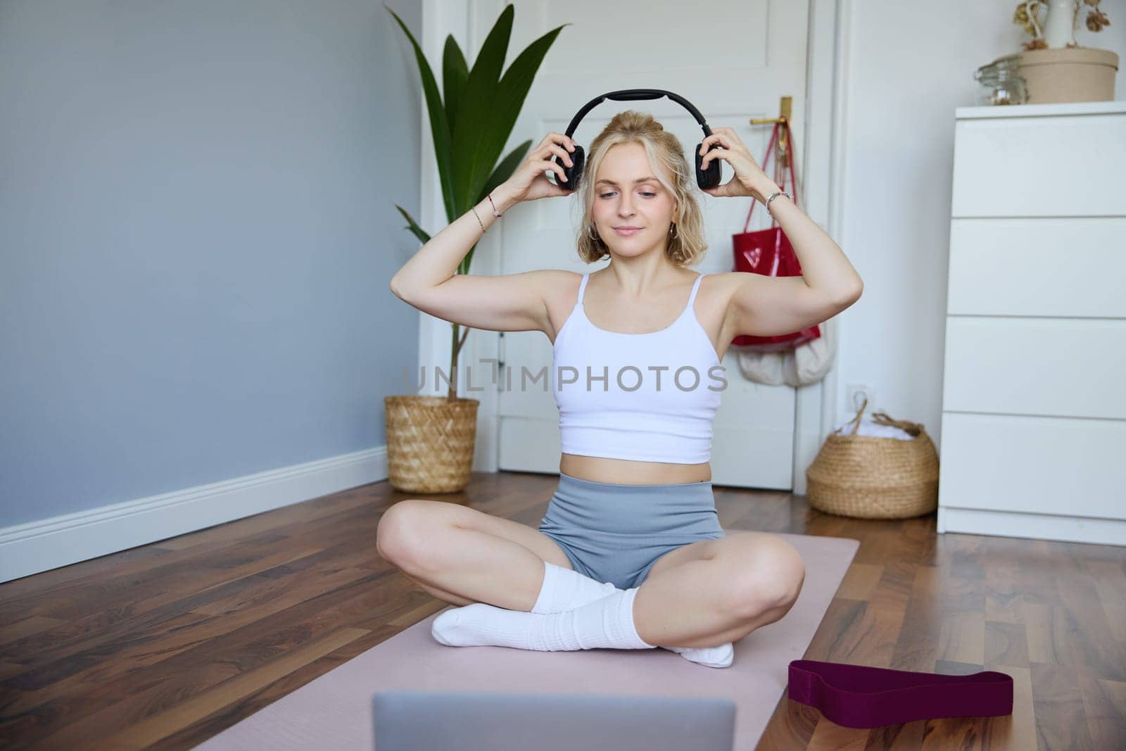 Portrait of young fitness girl, woman workout at home, listens to fitness instructor in wireless headphones, follows exercises on laptop.