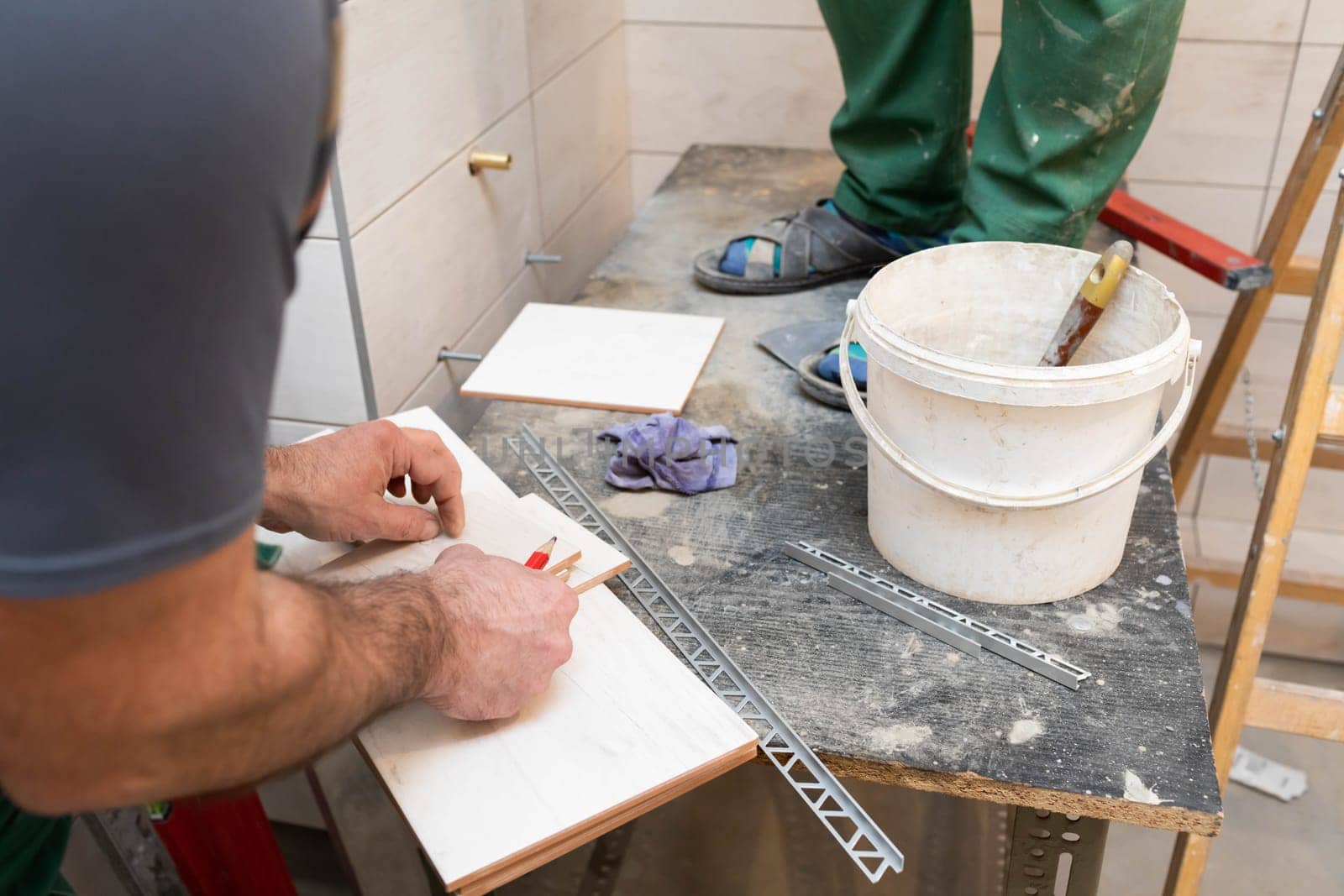 The builder measures the distance on the ceramic tile using a measuring tape. Distance measurement while the tiler is working.