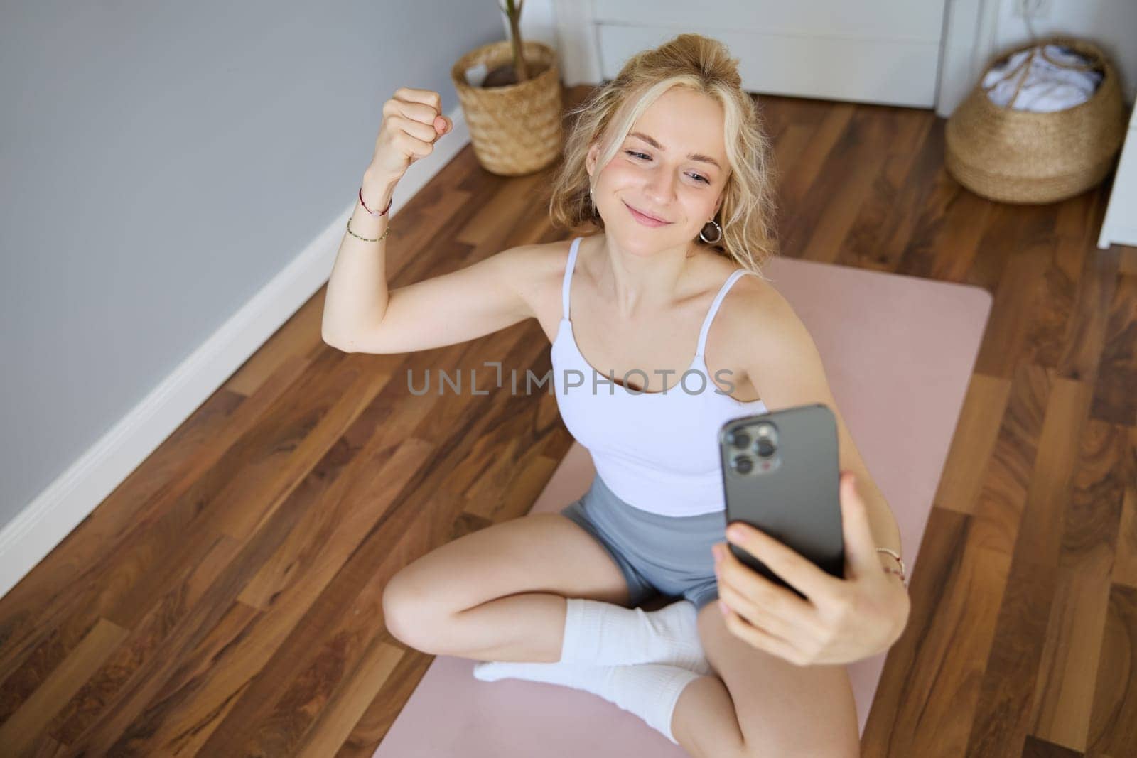 Portrait of young sporty woman taking selfie during workout training, content creator takes photos, shows muscles on camera, flexing biceps.