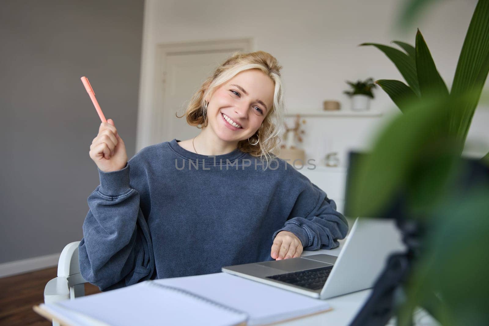 Portrait of young smiling woman, student talking to teacher online via video chat, doing course, attends remote course in internet, making notes.
