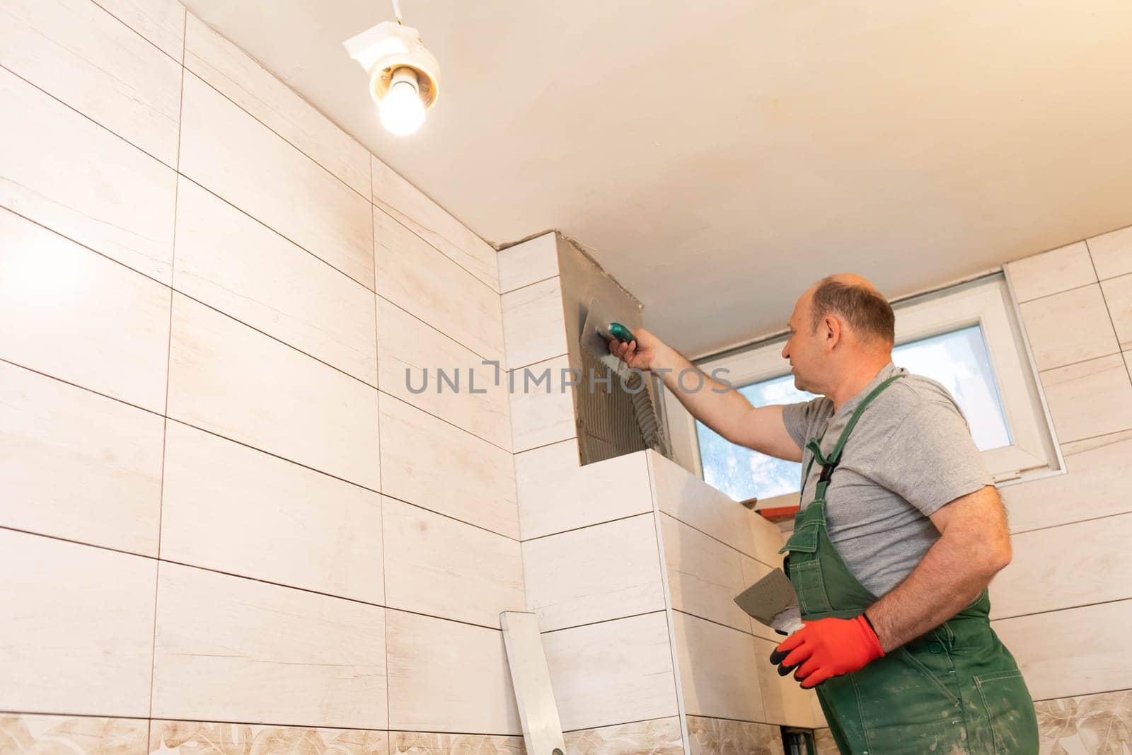 Applying cement glue to the wall with a special stainless steel trowel with teeth. An experienced construction worker.