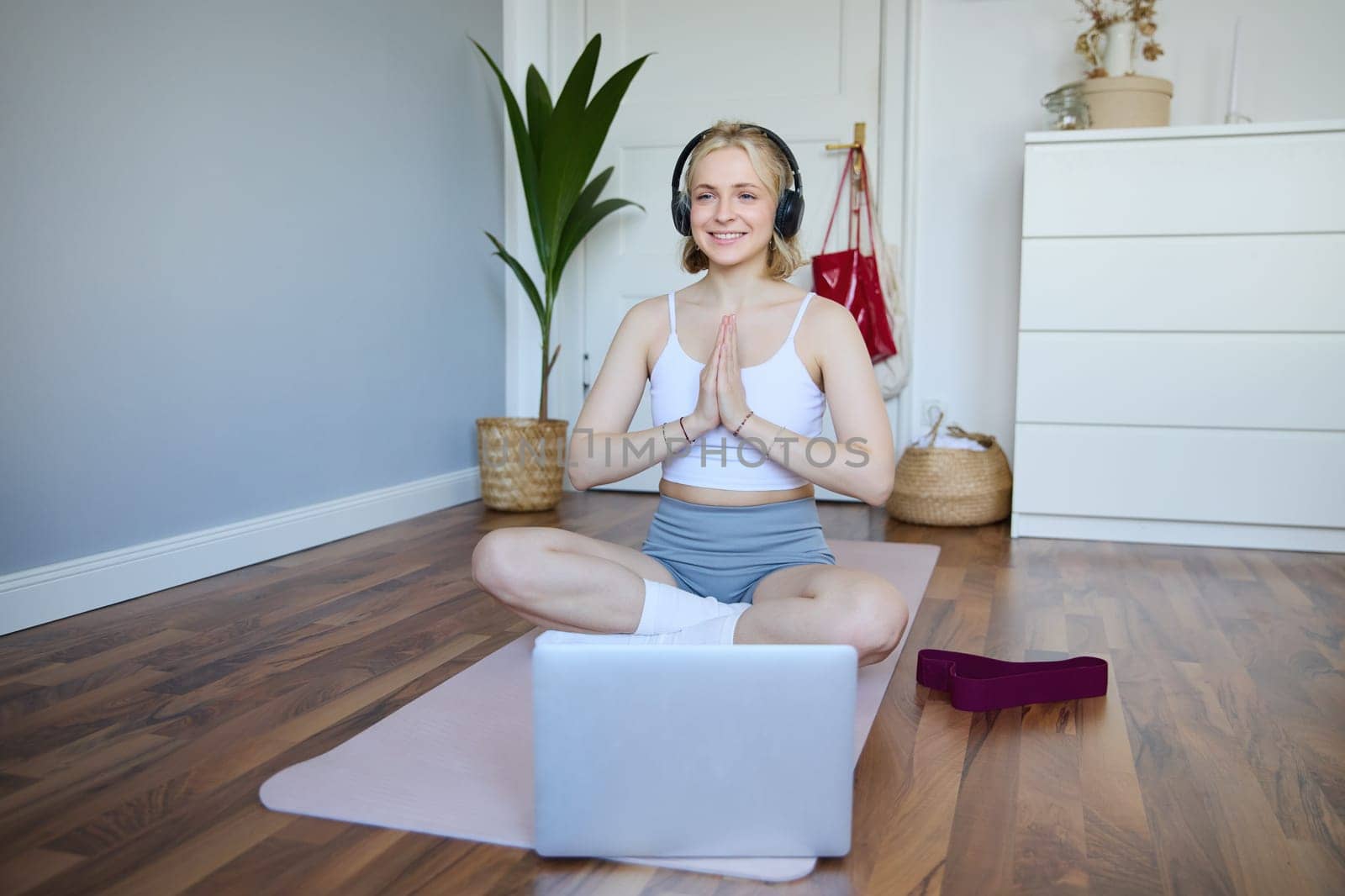 Portrait of blond young woman meditating, practise yoga, using yoga podcast to workout at home, sits on rubber mat.