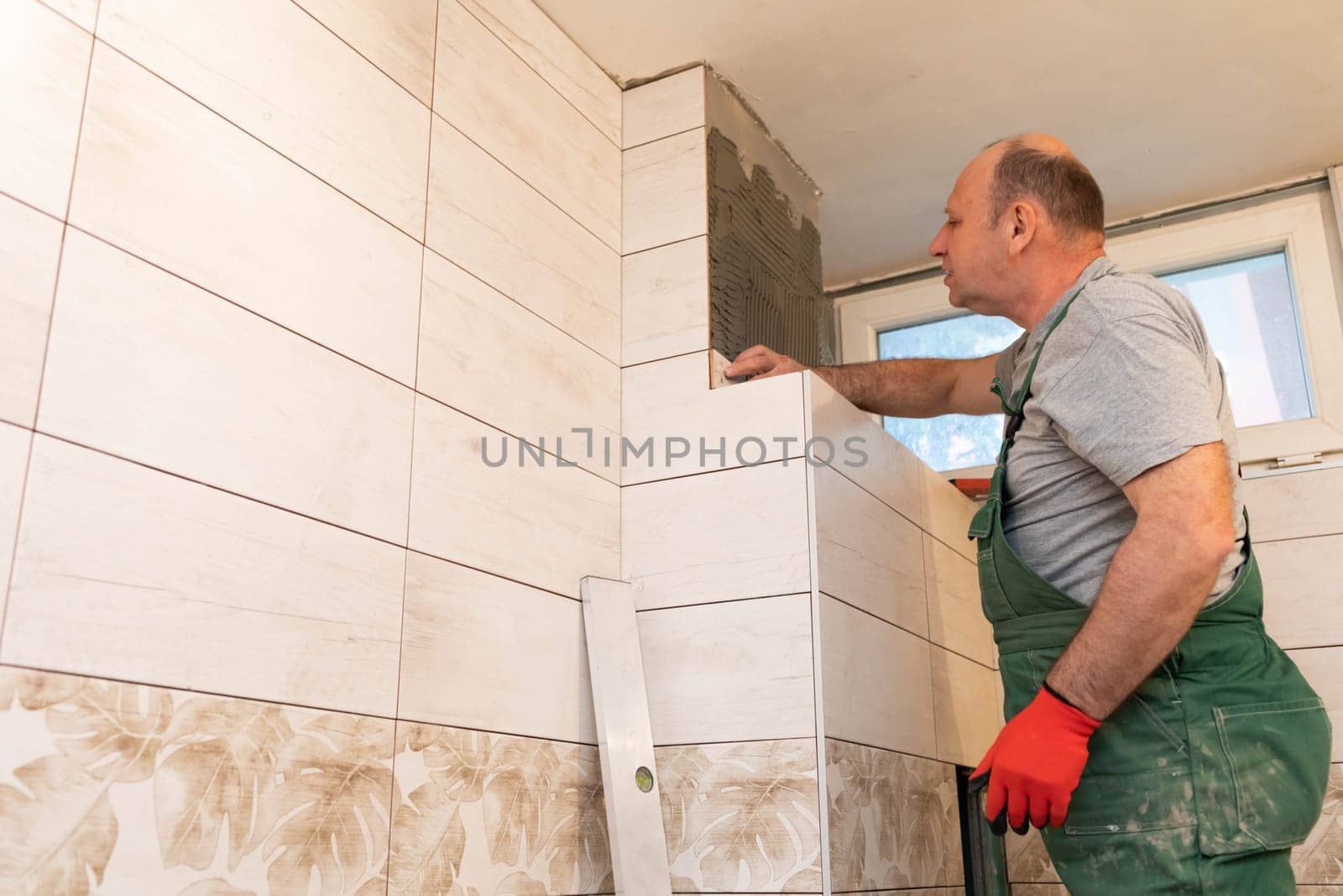 A middle-aged employee deals with laying tiles on the wall in the bathroom. An experienced construction worker.