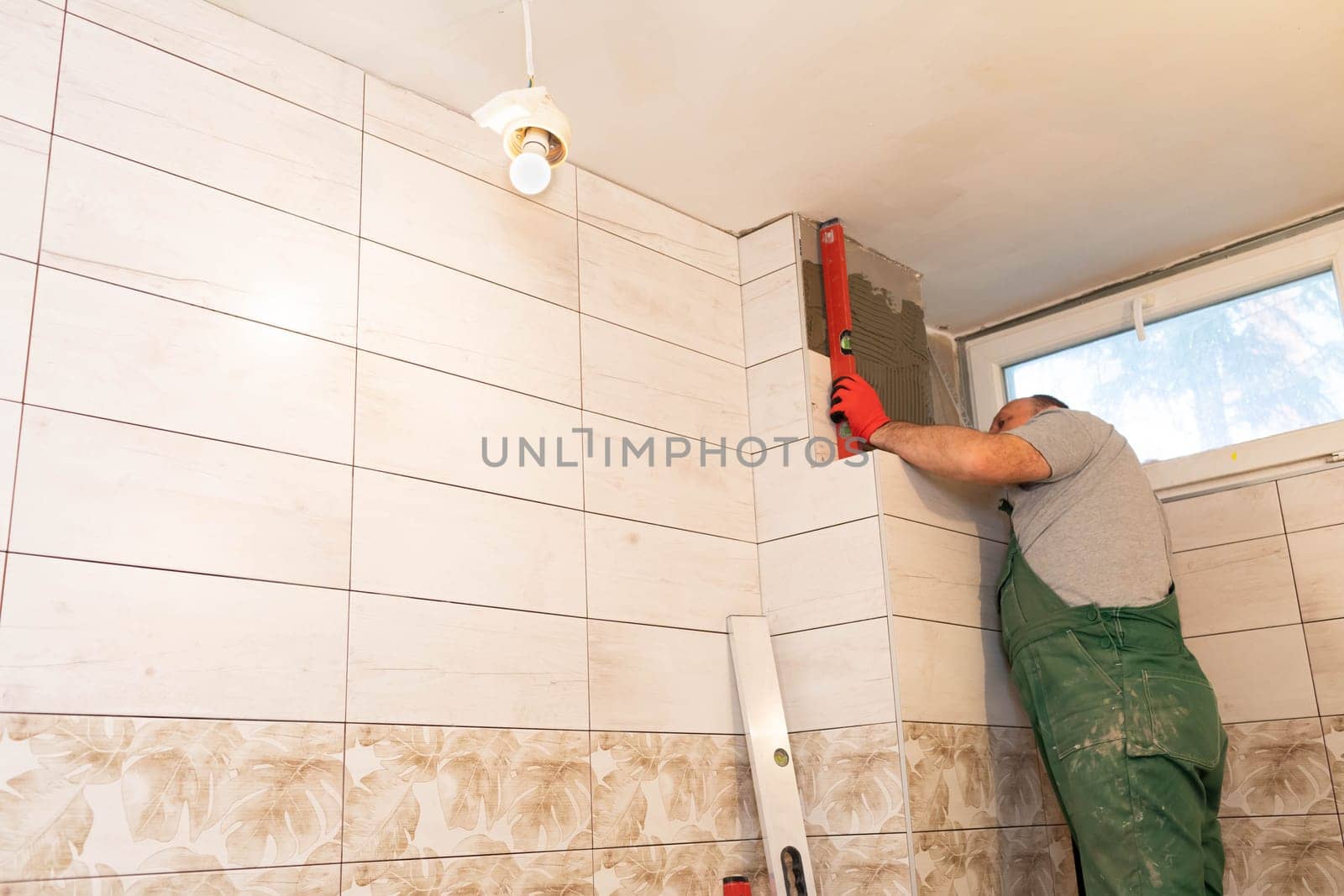 Using a spirit level, the employee checks the plumb and evenness of the entire plane of the glaze placed on the bathroom wall.
