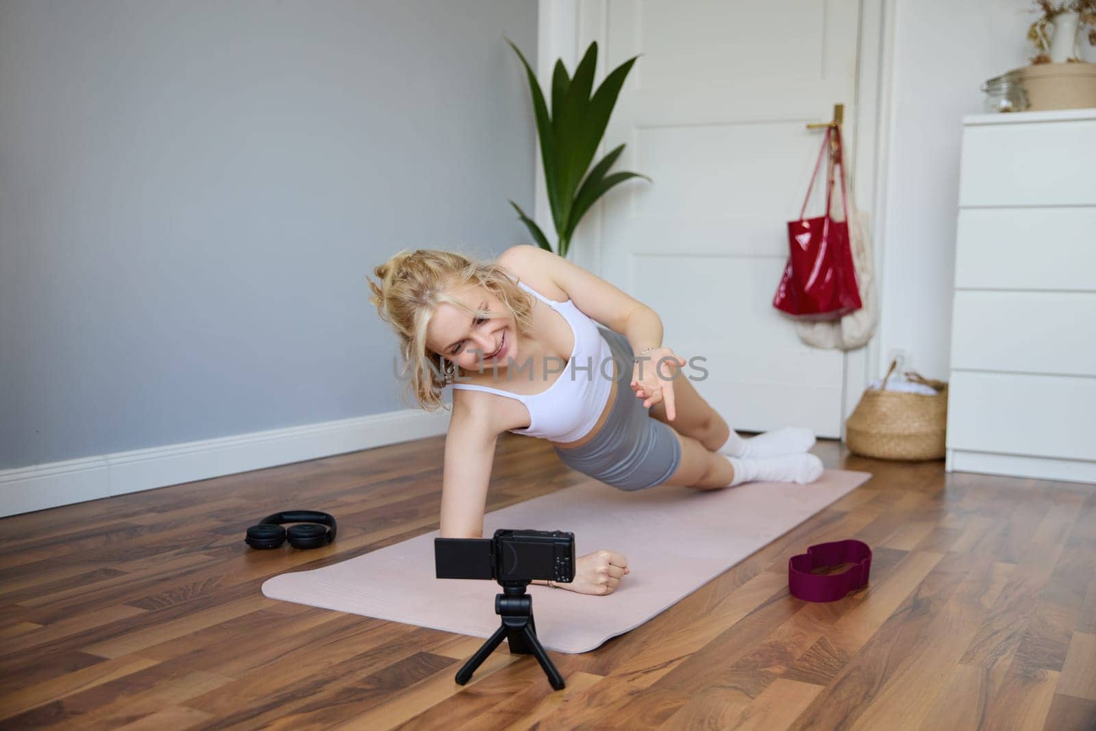 Portrait of fit and healthy young vlogger, fitness instructor woman standing in side plank, recording online lesson for clients on digital camera, shooting video about workout.