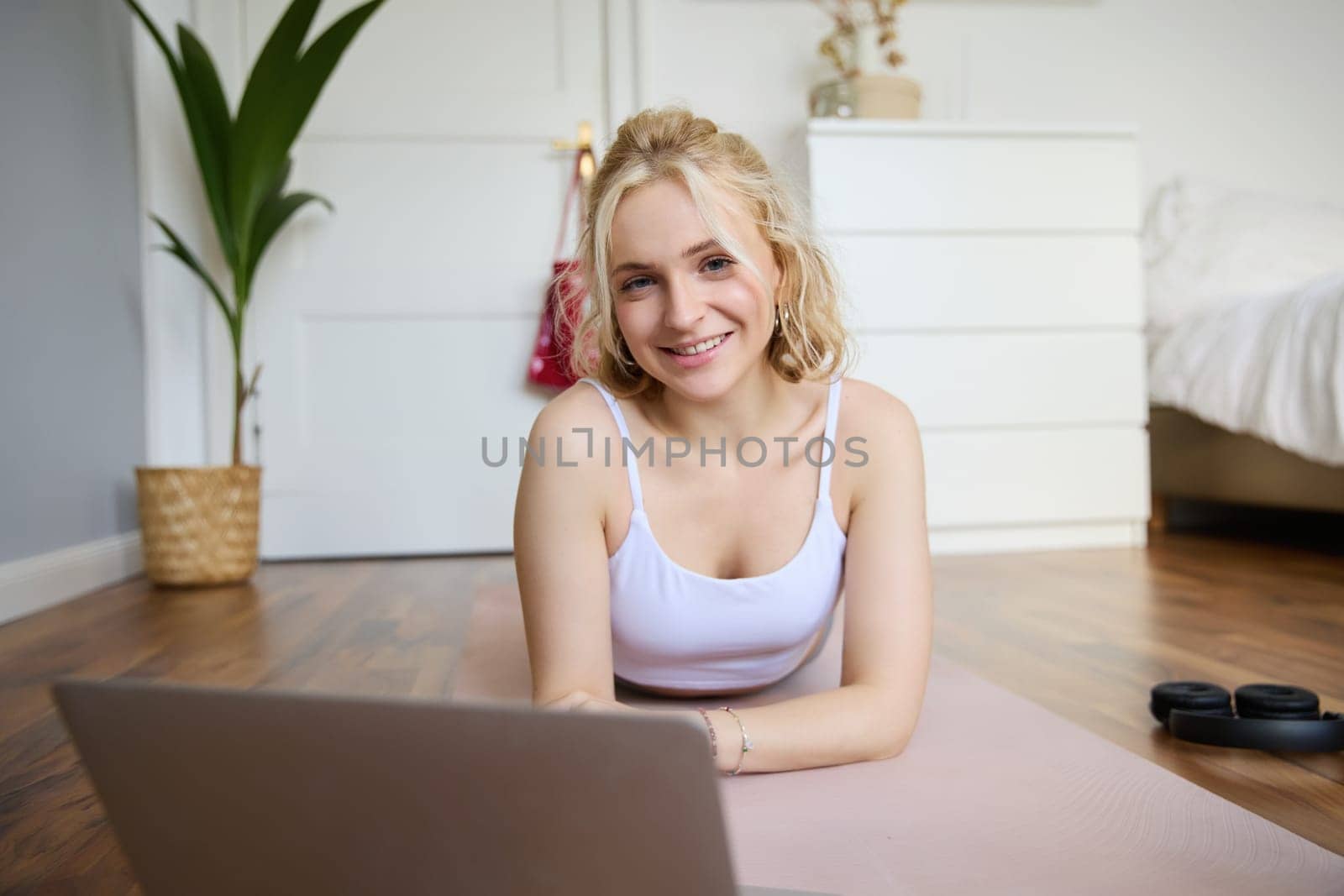 Portrait of cute young fitness woman, doing workout at home, lying on rubber yoga mat, watching exercises online on laptop.