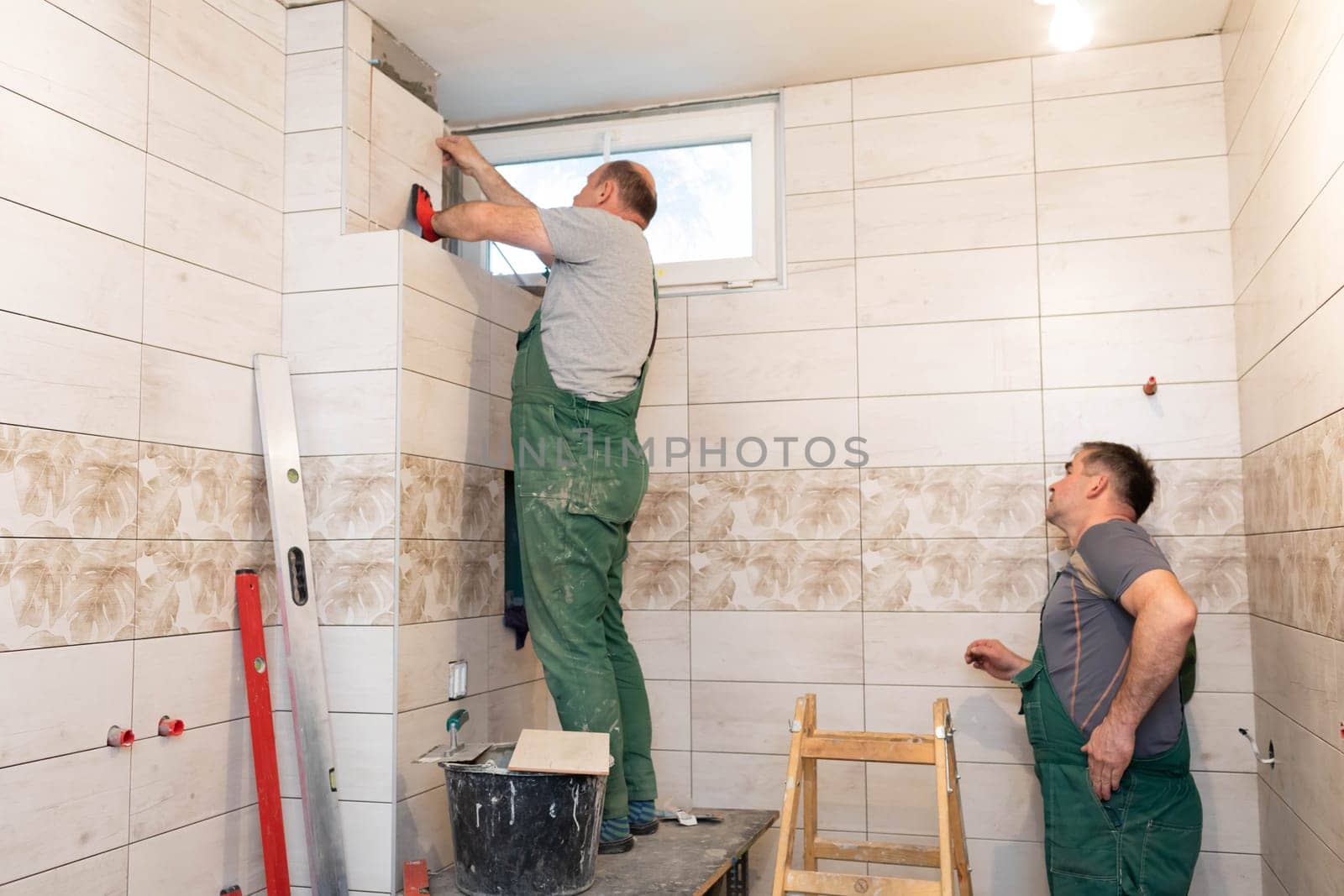 A middle-aged employee deals with laying tiles on the wall in the bathroom. An experienced construction worker.