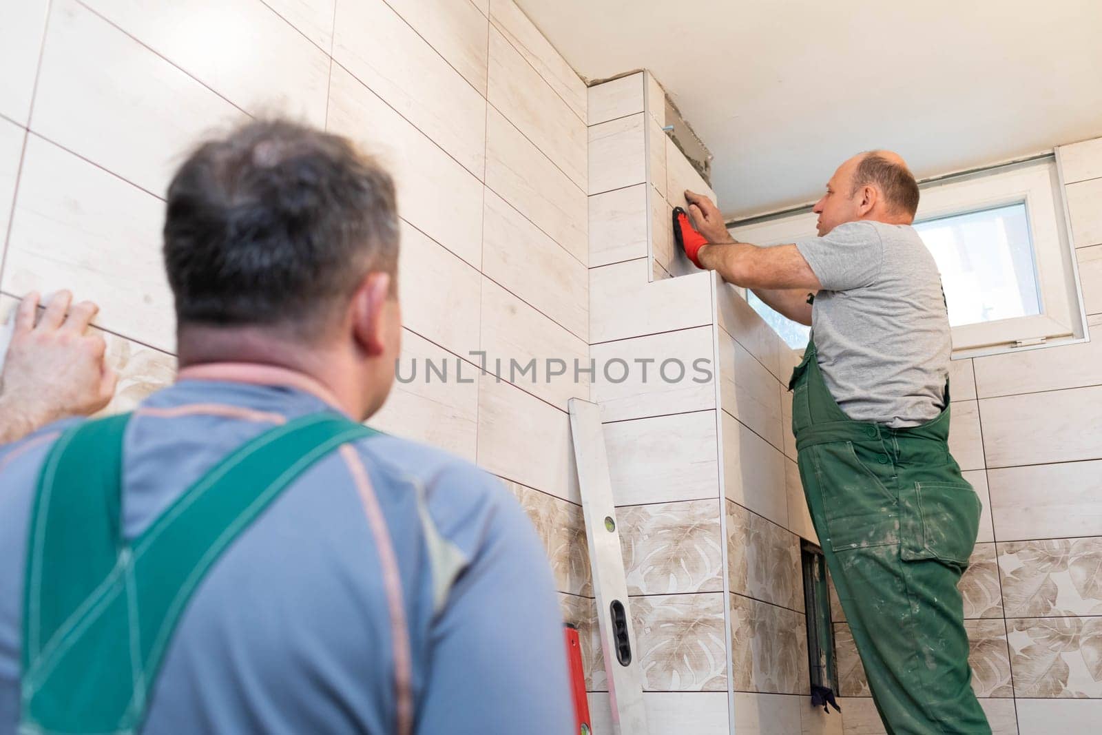 A middle-aged employee deals with laying tiles on the wall in the bathroom. An experienced construction worker.