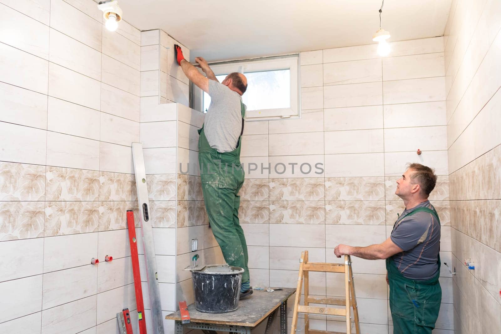 A middle-aged employee deals with laying tiles on the wall in the bathroom. An experienced construction worker.