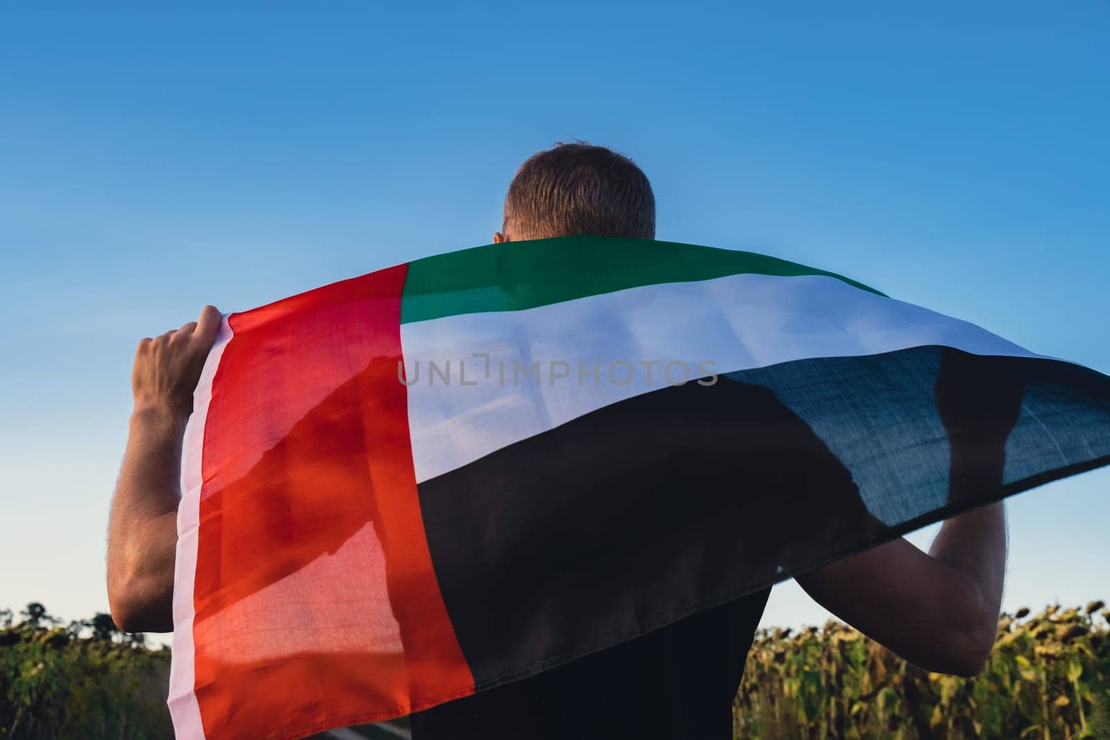 Man holding National Flag Of UAE Waving In The Wind sunset. Flag of United Arab Emirates on Sun Background. Sign of Dubai. Spirit of the Union National Independence Day by anna_stasiia