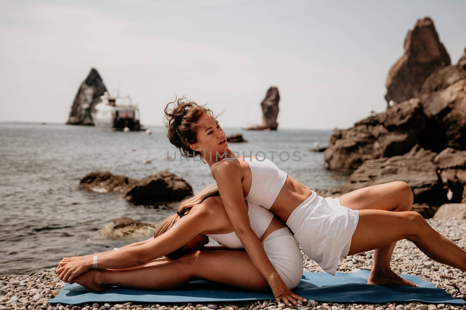 Woman sea yoga. Two Happy women meditating in yoga pose on the beach, ocean and rock mountains. Motivation and inspirational fit and exercising. Healthy lifestyle outdoors in nature, fitness concept. by panophotograph