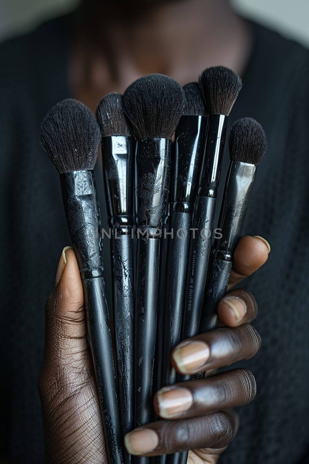 Hand holding a collection of makeup brushes, symbolizing artistry and beauty tools.