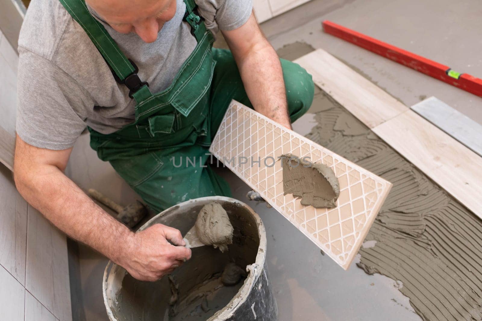 A construction worker lubricates the bottom of the ceramic tile with a metal trowel with special glue.