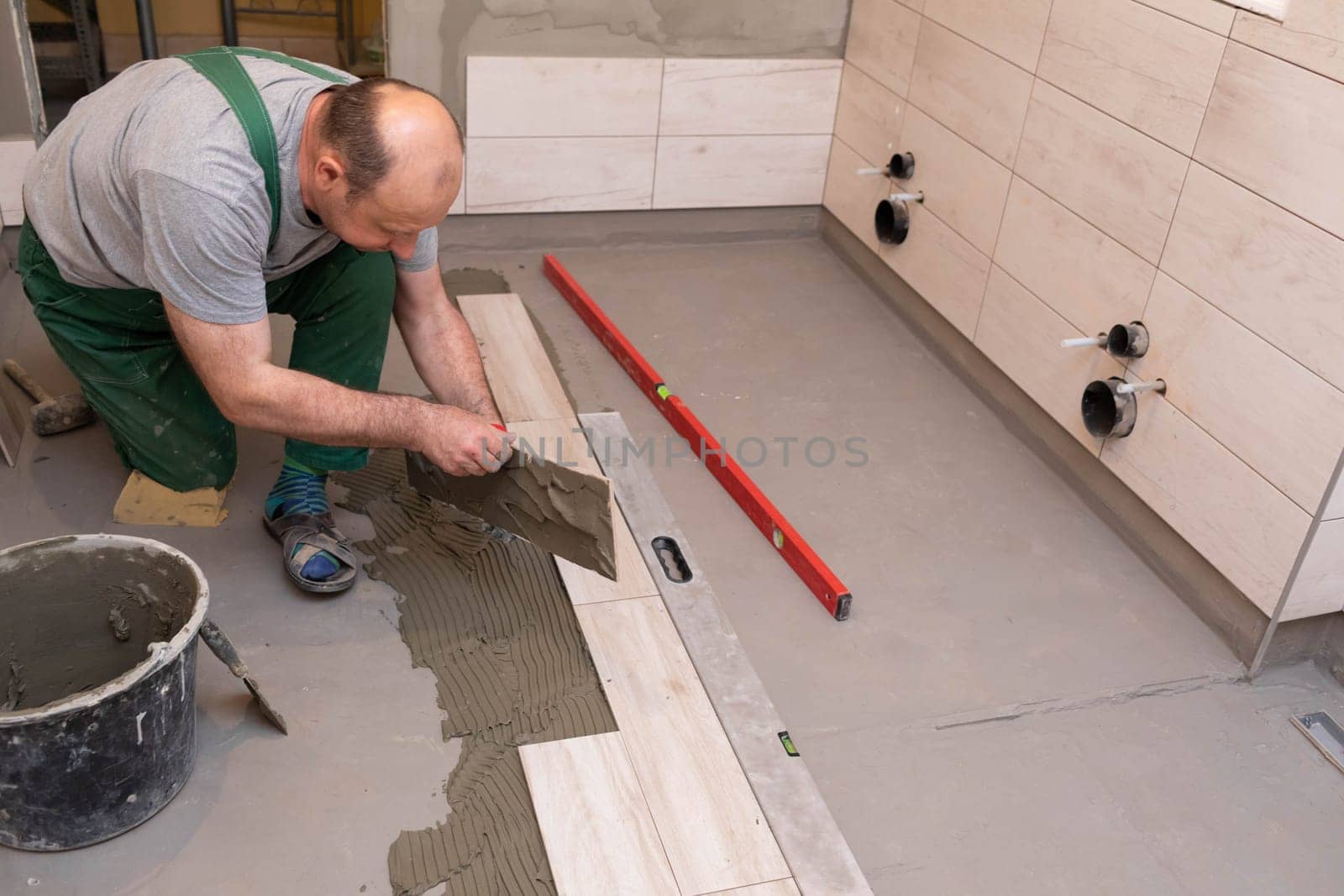 General construction worker. Adhesive for ceramic tiles. The builder glues terracotta to the floor.