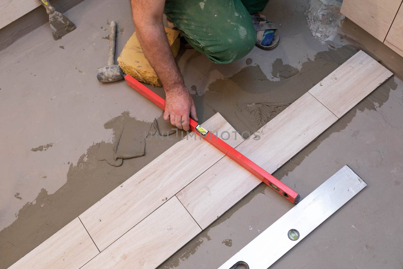 Spirit level - a device for checking the correctness of works performed in relation to the level. A professional construction worker. Kneeling.