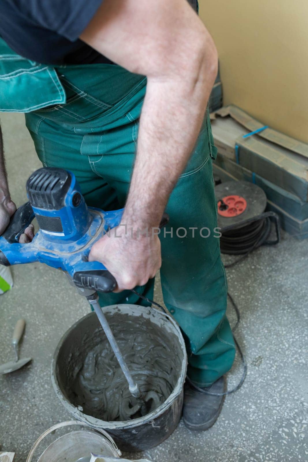Electric stirrer. Mixing cement based adhesive. A professional construction worker. A bucket full of crushed adhesive for ceramic tiles.